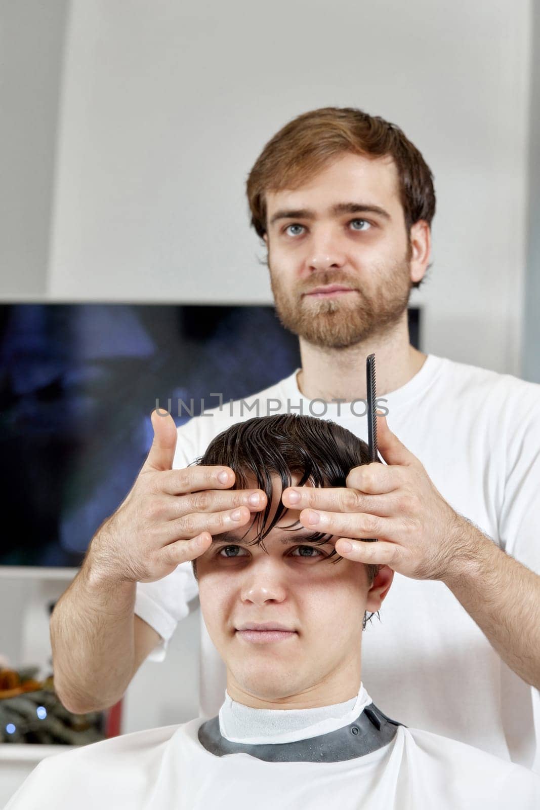 Cheerful barber combing caucasian man while sitting in chair before haircut at barbershop. client tells what haircut he wants