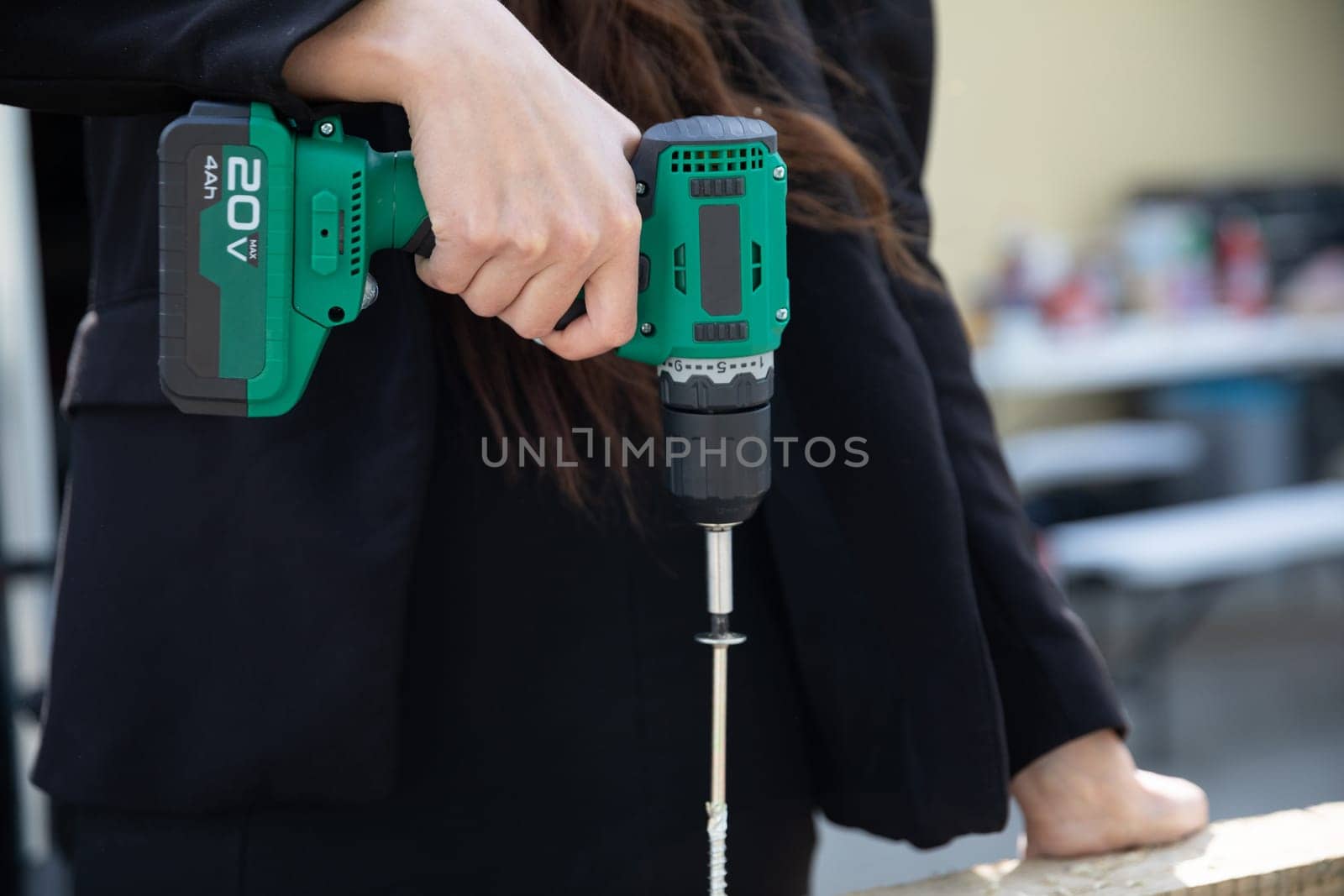 Driving a large screw with a cordless screwdriver. A woman holds a power tool in her hand.