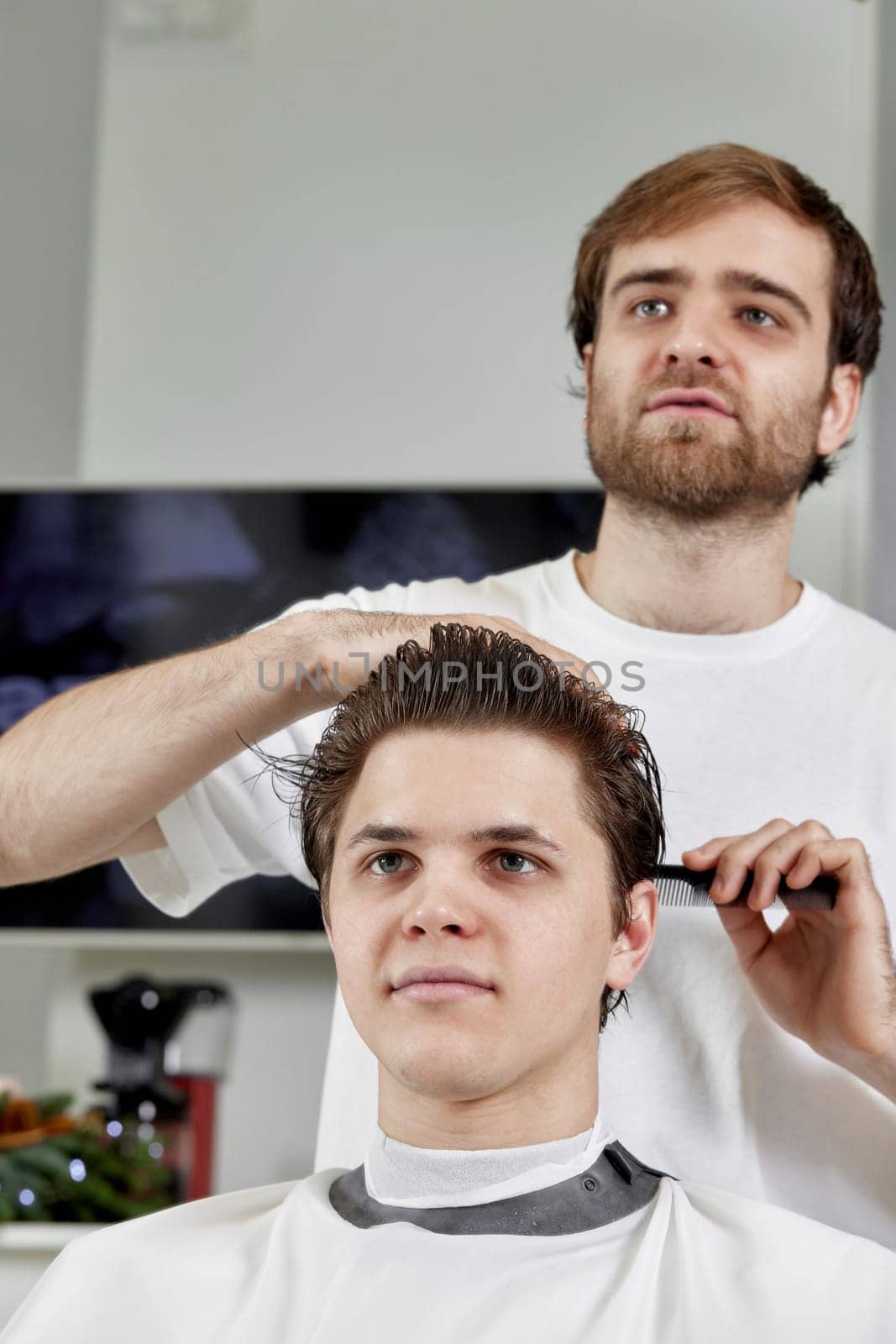 friendly barber combing caucasian man while sitting in chair before haircut at barbershop. client tells what haircut he wants