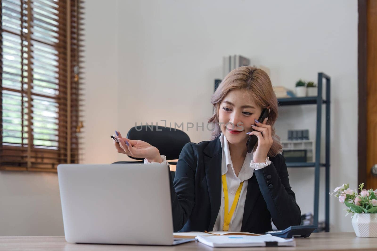 Happy young asian woman talking on the mobile phone and working smiling while sitting at her working place in office.