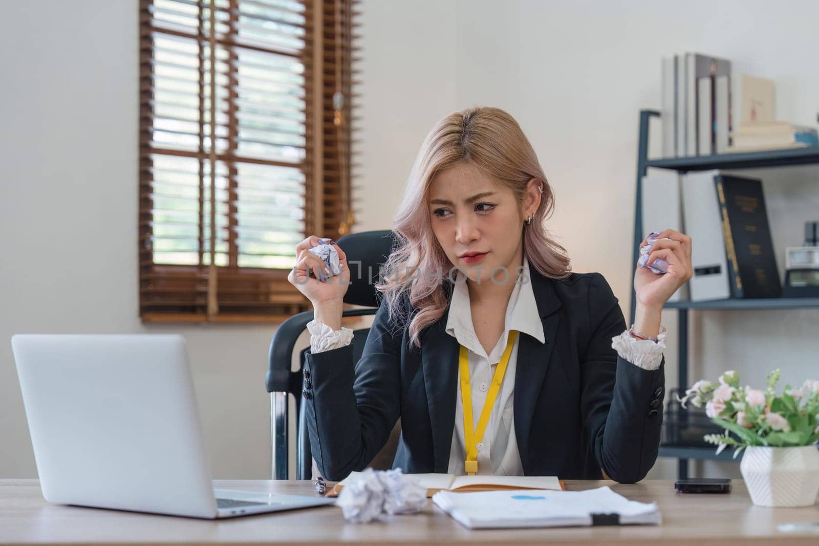 Businesswoman tired and stressed with overworked at desk, woman asian with worried not idea with graph analysis laptop and crumpled paper at office.