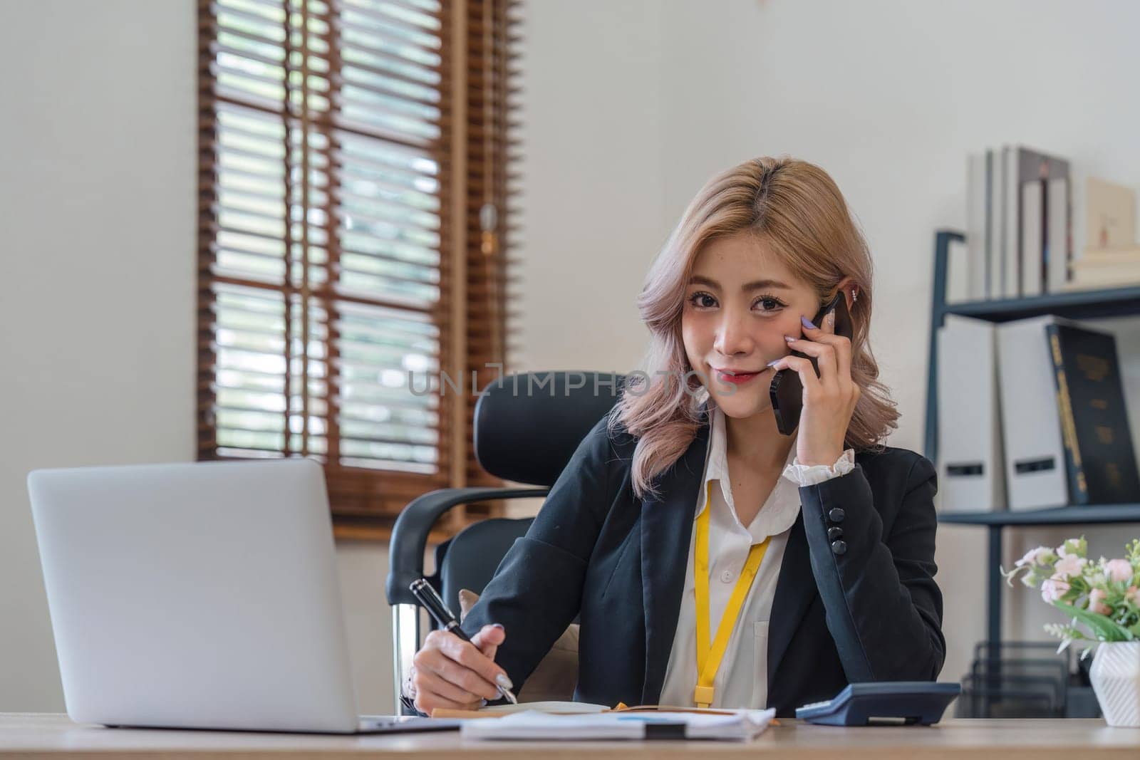 Happy young asian woman talking on the mobile phone and working smiling while sitting at her working place in office.