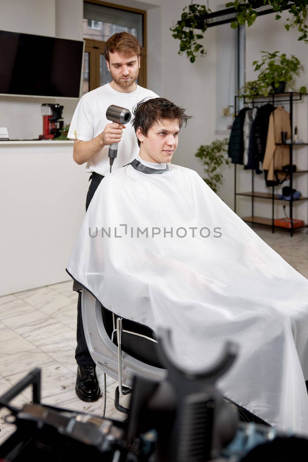 Professional hairdresser during work with man client with hair dryer by erstudio