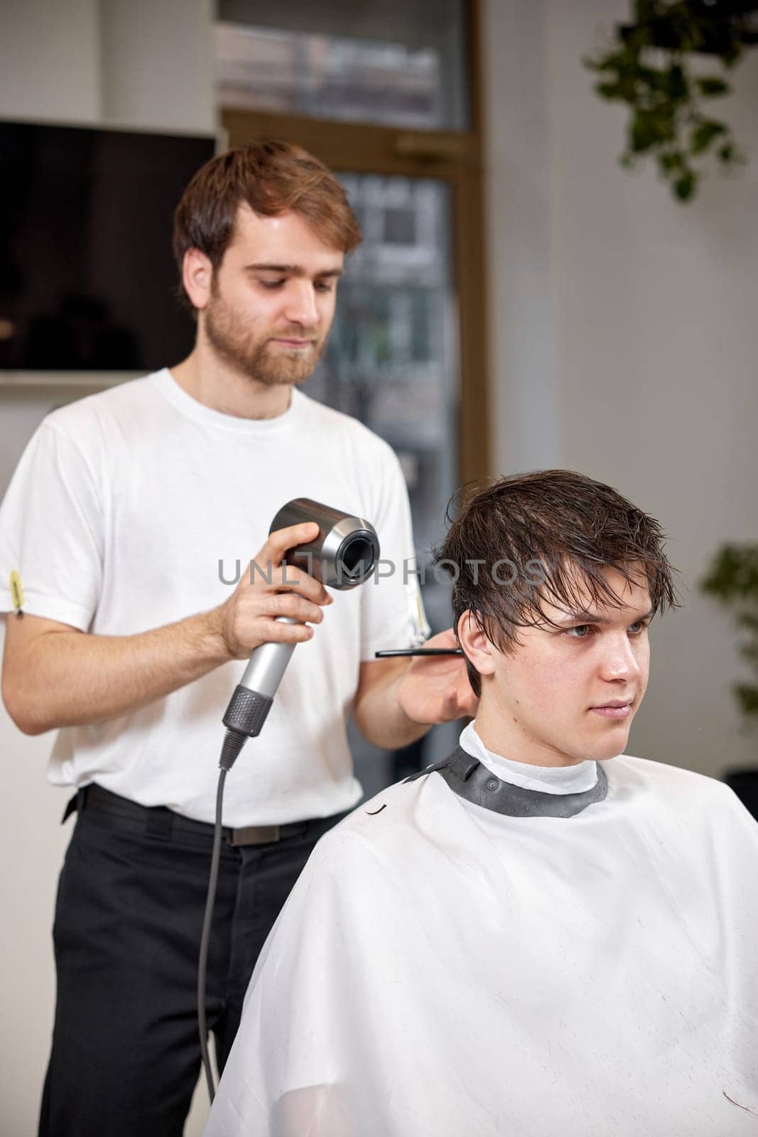 Professional hairdresser during work with man client with hair dryer in barber shop. Haircut in the barbershop.