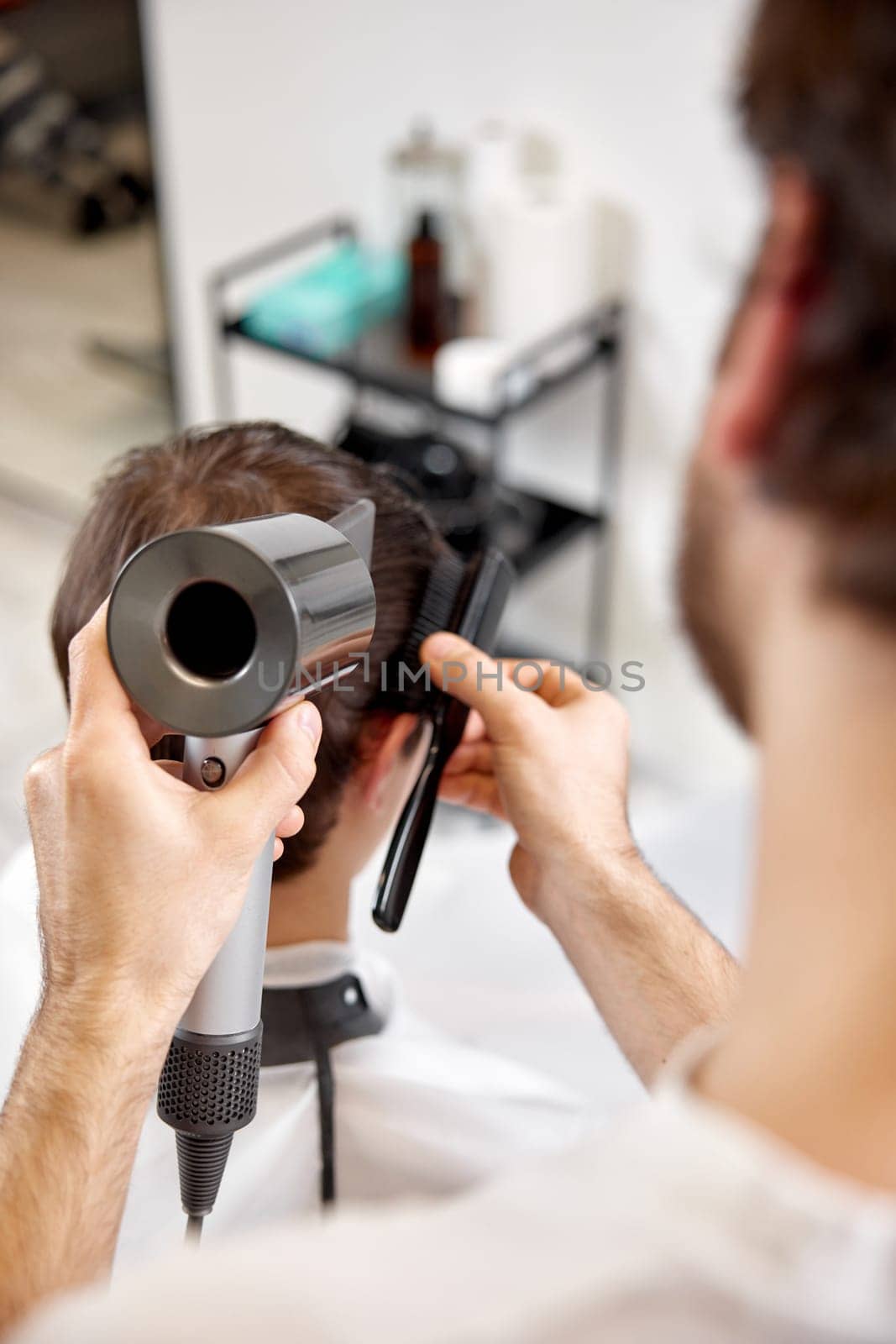 Professional hairdresser using hair dryer and hairbrush of his client in barber shop. Haircut in the barbershop.