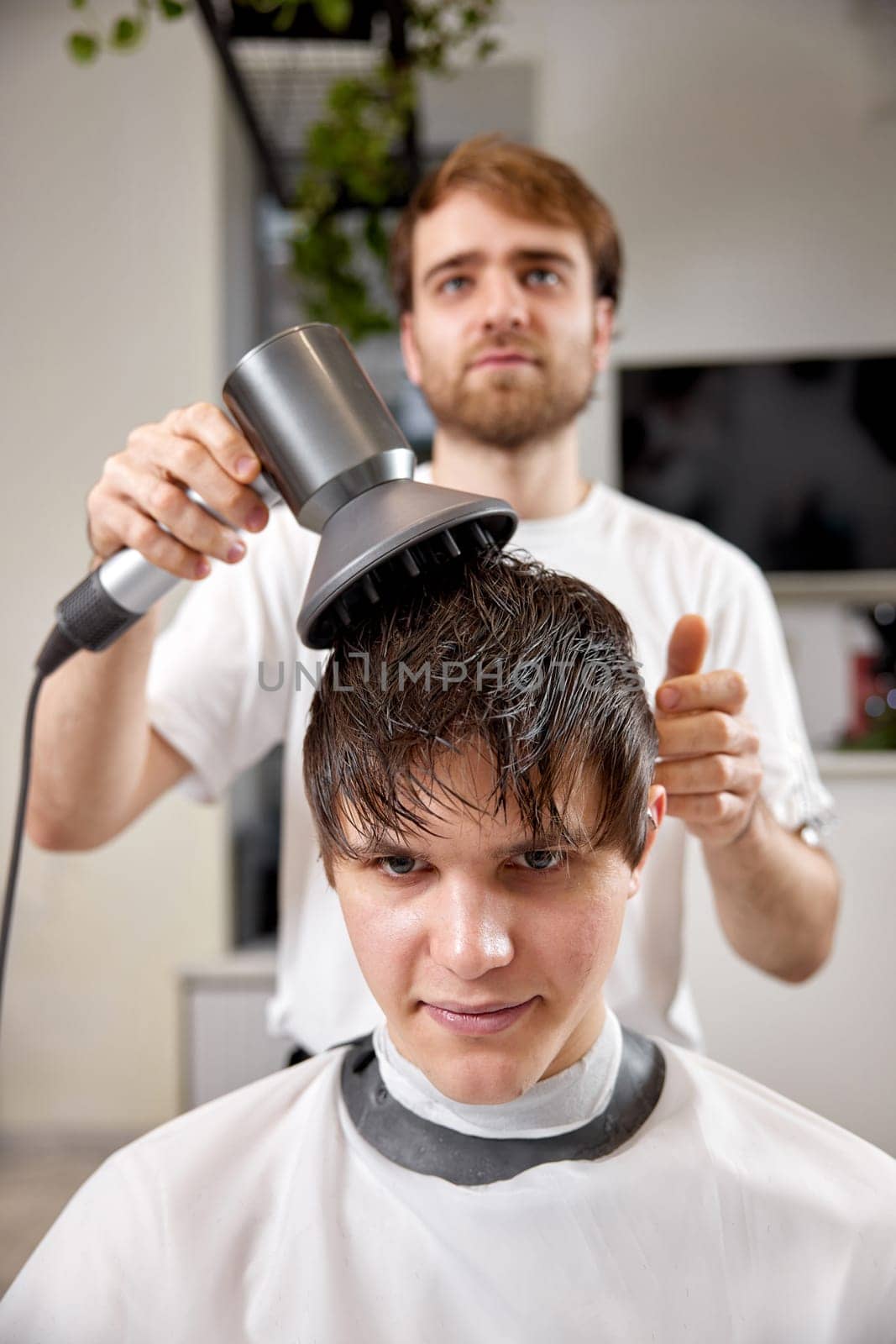 Professional hairdresser using hair dryer and hairbrush of his client in barber shop. Haircut in the barbershop.