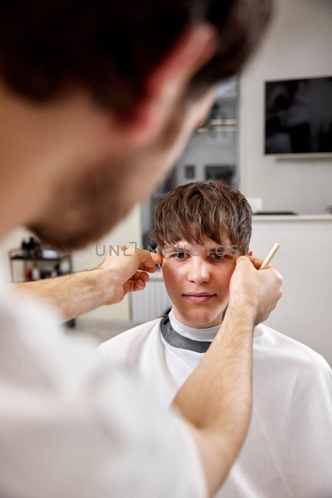 young caucasian man getting haircut by professional male hairstylist at barber shop.