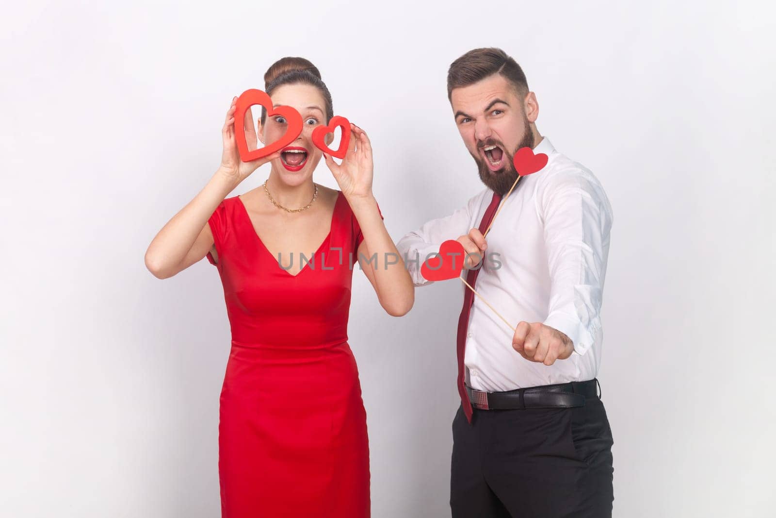 Crazy man and amazed woman in red dress standing together, holding heart figures, being emotive. by Khosro1