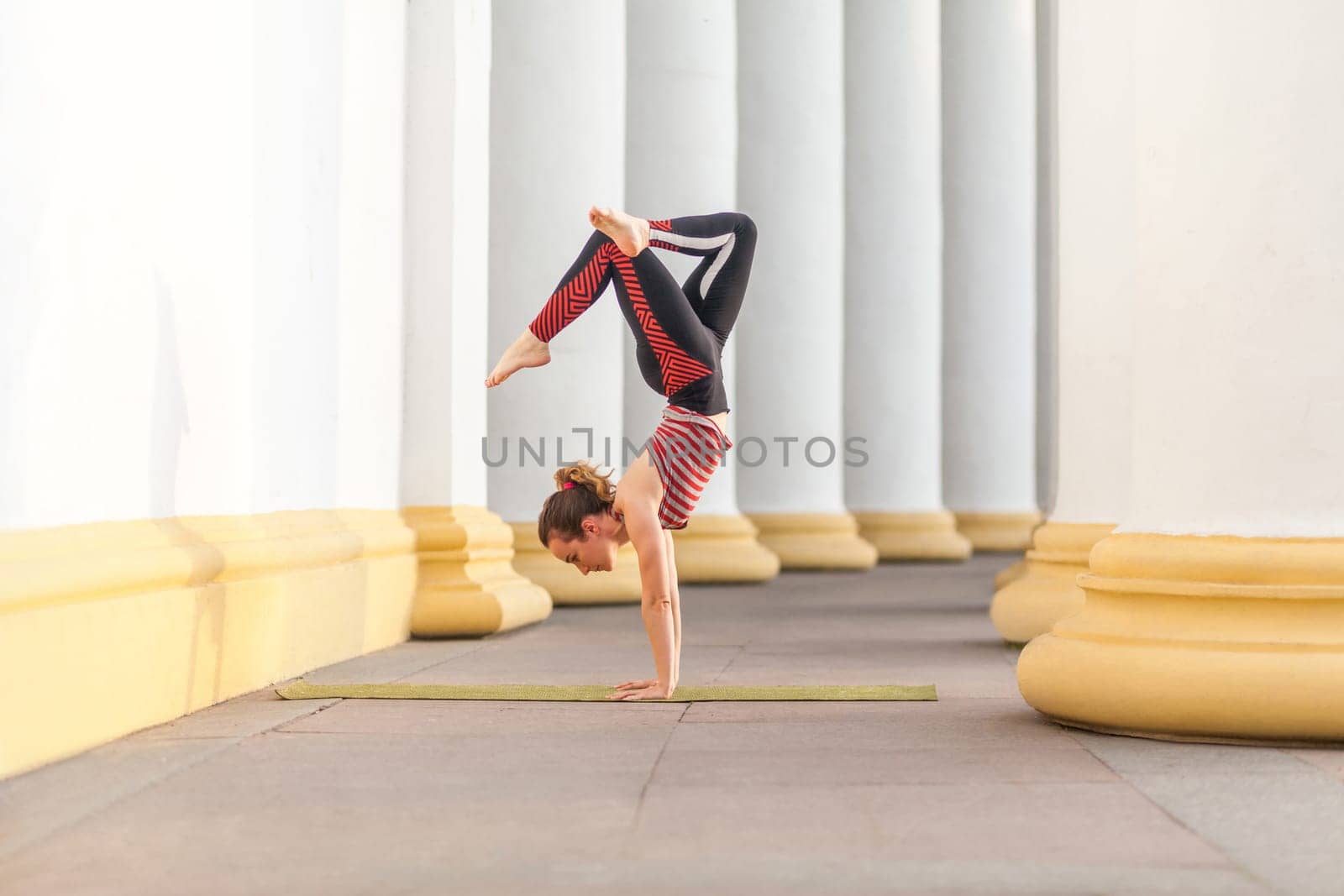 Woman in sporty pants and top practicing yoga outdoor, standing in crane, bakasana pose. by Khosro1