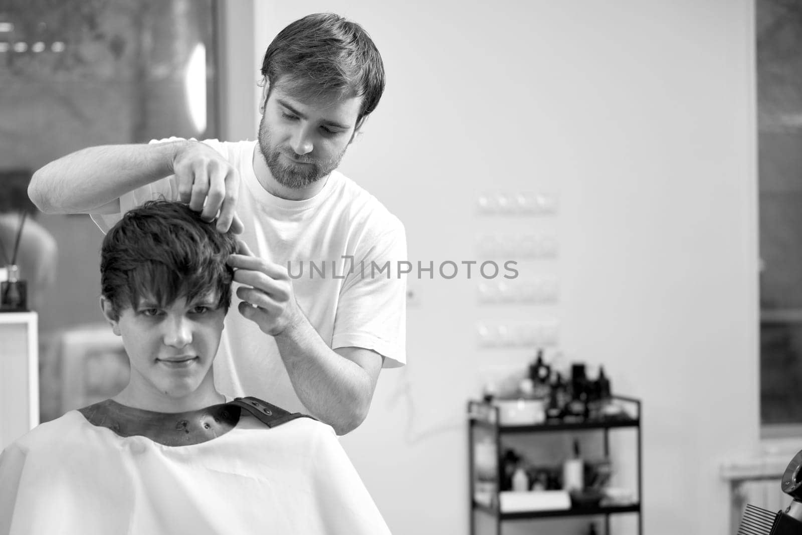young caucasian man getting haircut by professional male hairstylist at barber shop. black and white