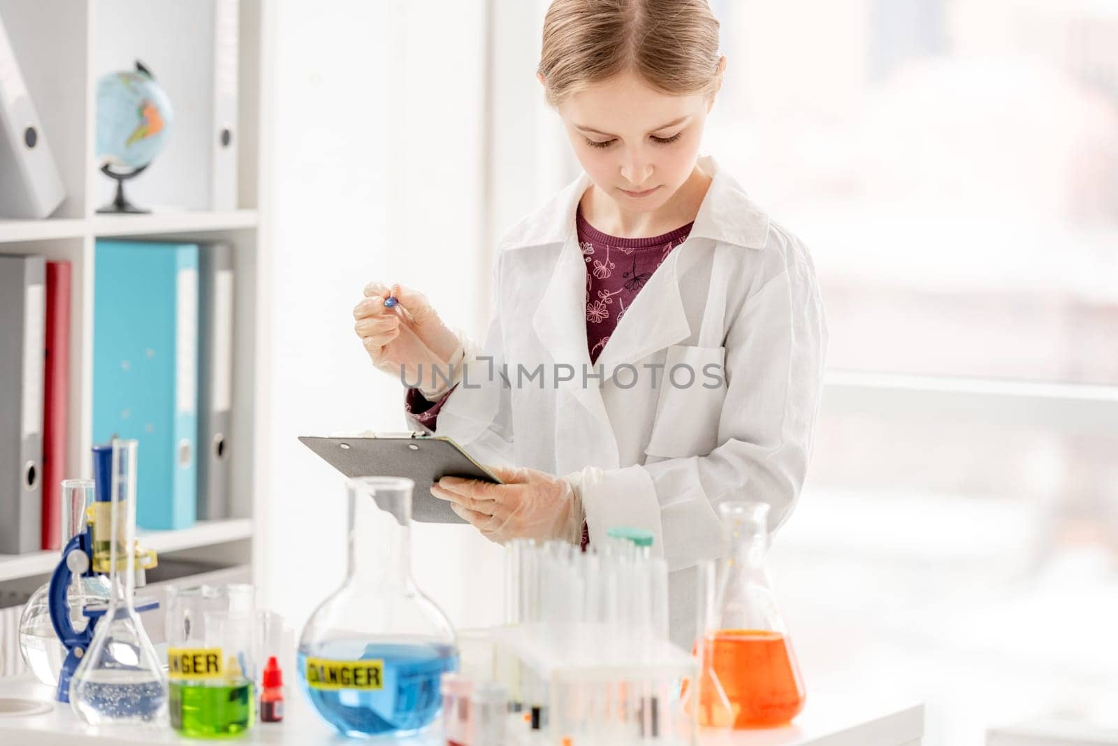 Girl during scientific chemistry experiment making notes close to table with tubes. Schoolgirl with chemical equipment on school lesson