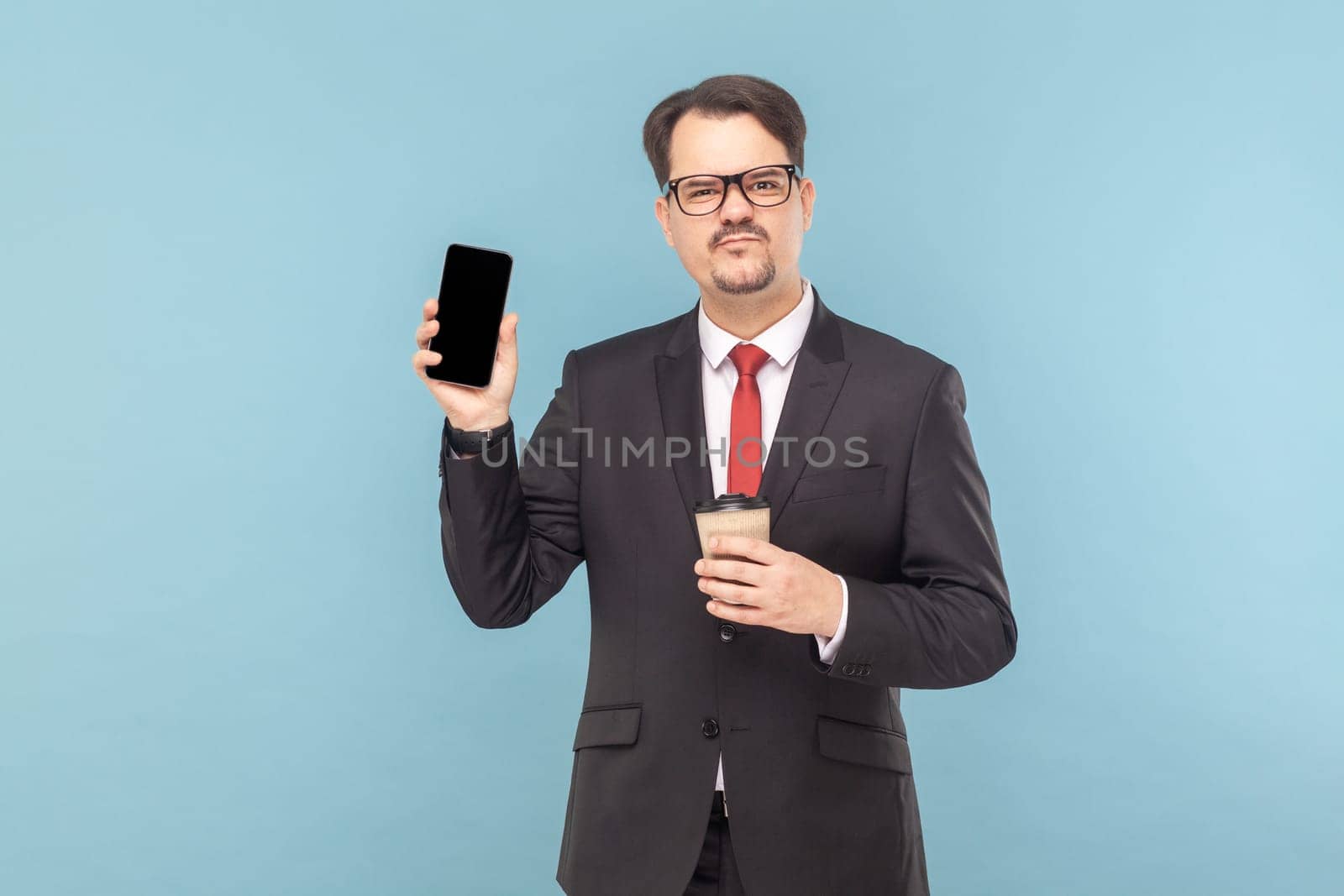 Sad man standing showing smart phone with blank screen, frowning face, drinking coffee to go. by Khosro1