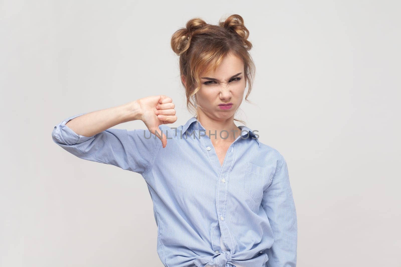 Woman shows disapproval sign, keeps thumb down, expresses dislike, frowning face in discontent. by Khosro1