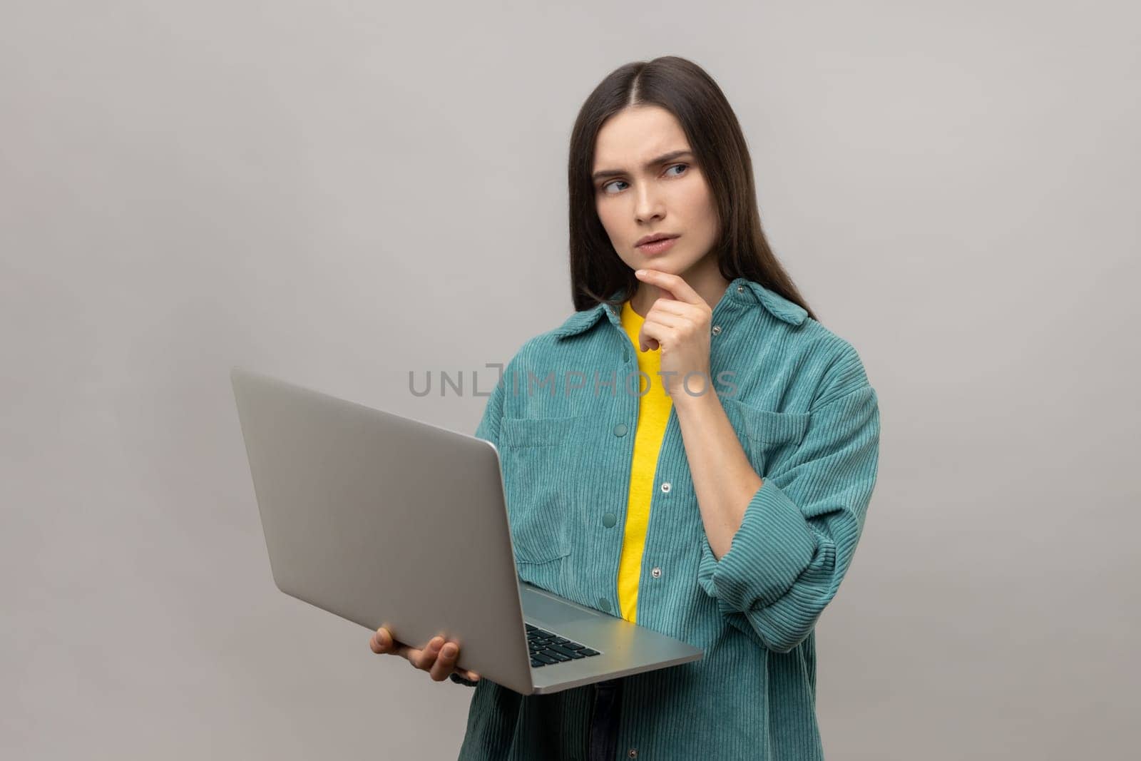 Pensive thoughtful smart dark haired woman holding laptop and thinking about school project. by Khosro1