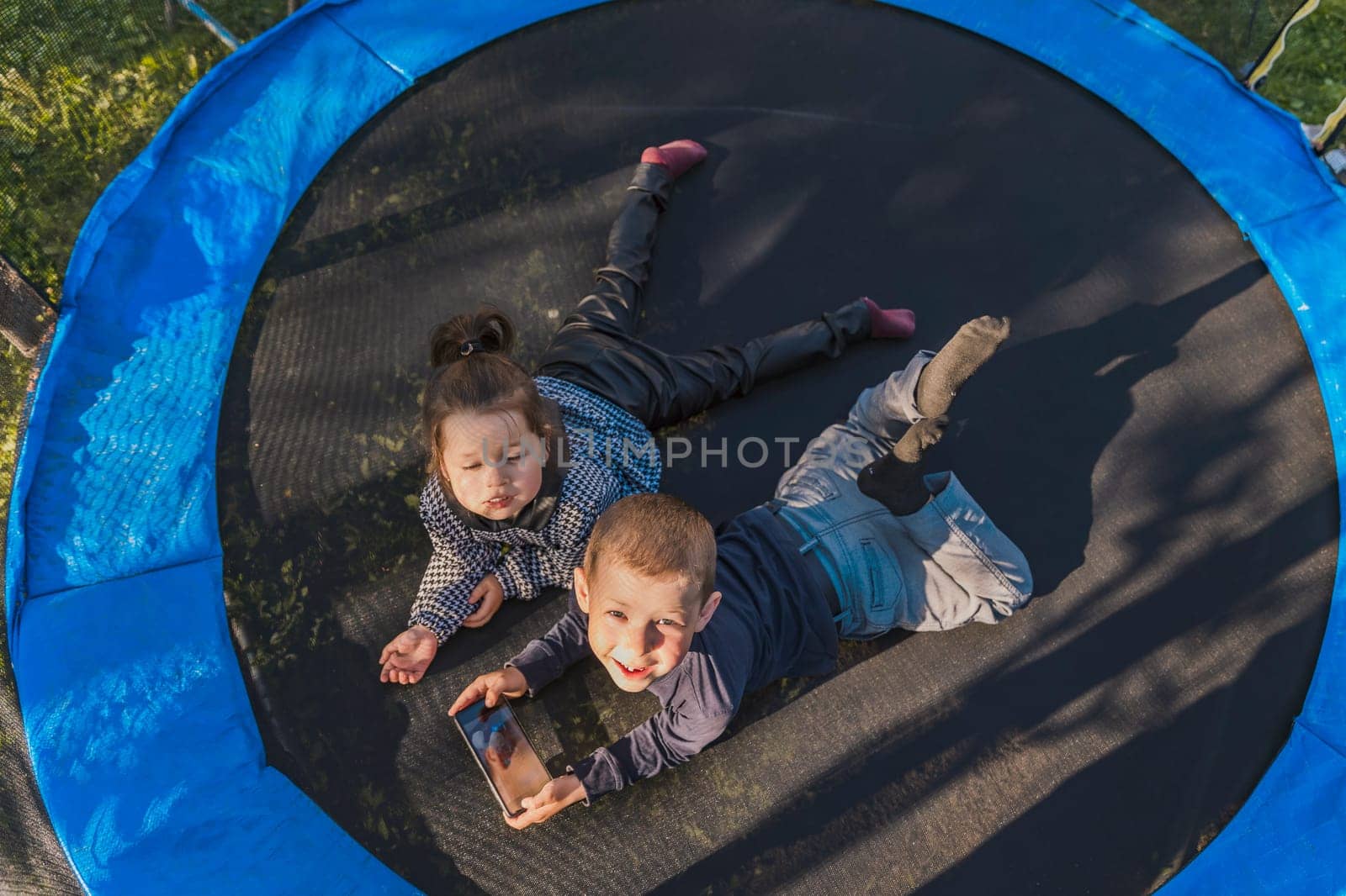 children look at the phone while lying on a trampoline, top view
