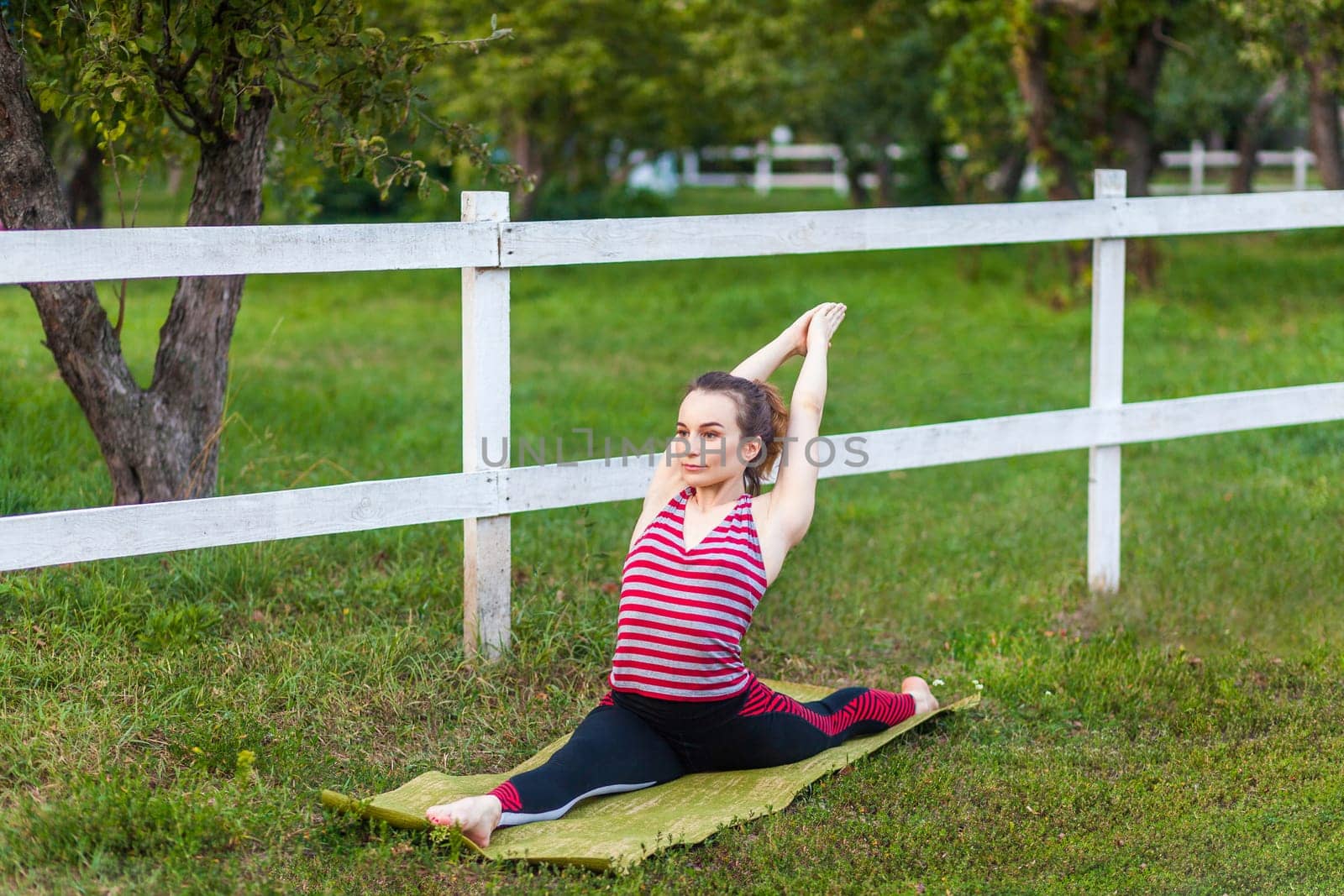 Hanumanasana pose. Full length portrait of yogi athletic beautiful woman practicing yoga in the park in open air, doing, Monkey God, sitting floor stretch split legs twine pose, wearing sportswear.