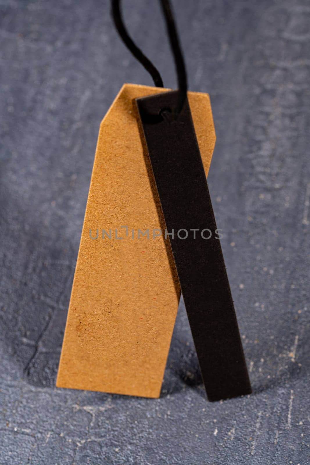 A vertical shot of a brown paper tag on a string with a thin black strip of cloth