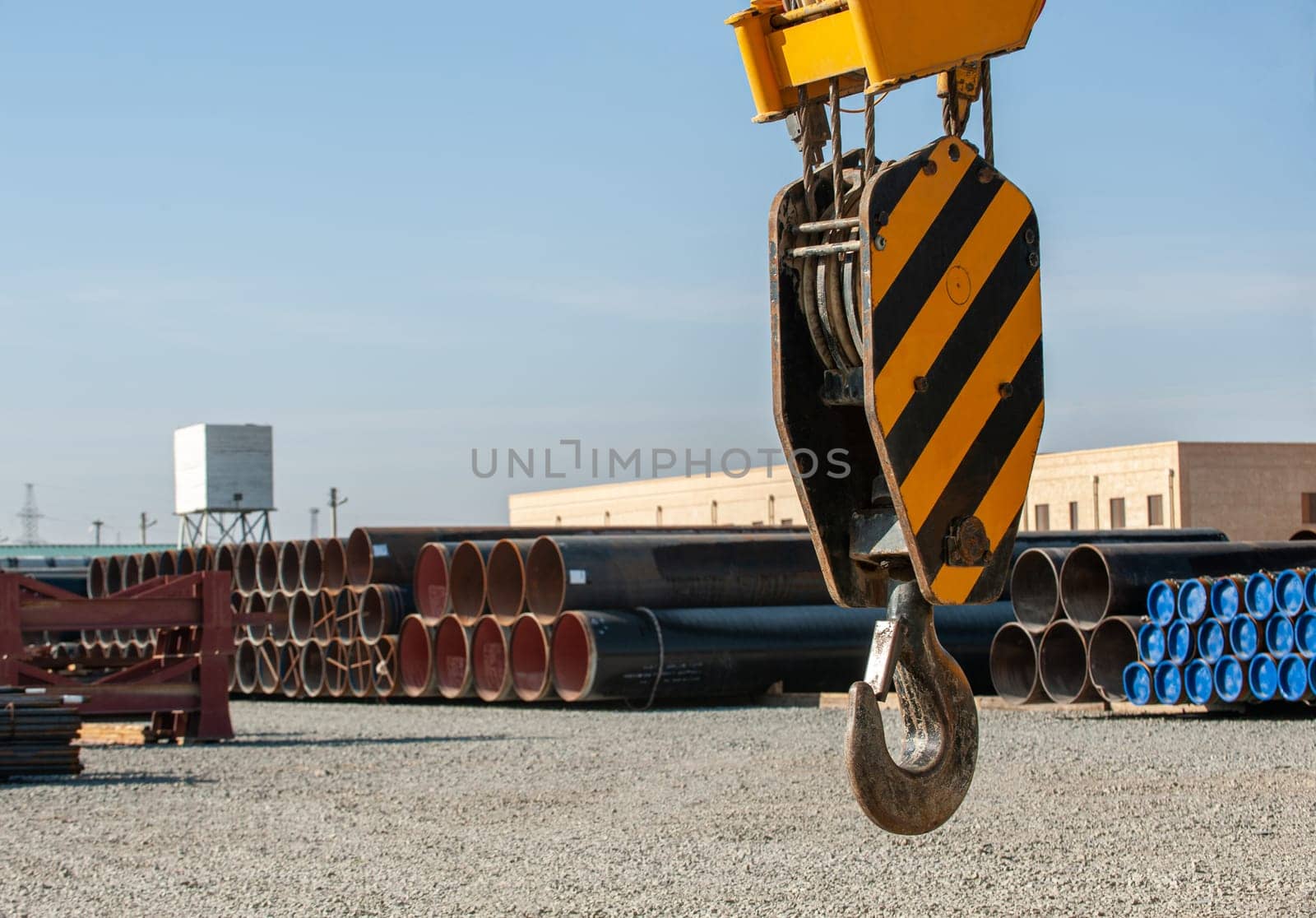 A close-up of a construction crane hook against the background of a site with oilfield pipes