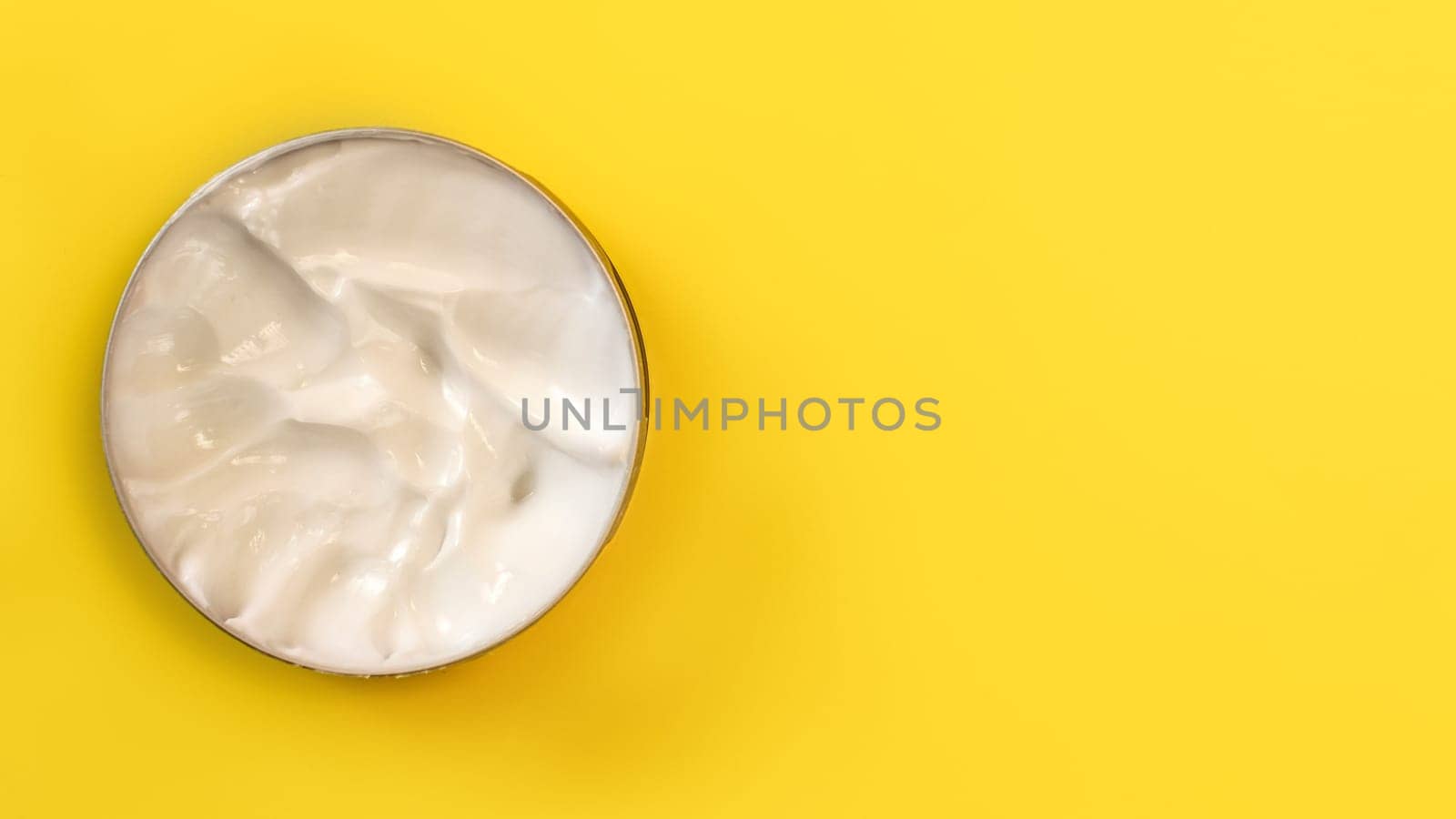 Top view - cosmetic cream in metal tin on yellow board. Space for text on the right