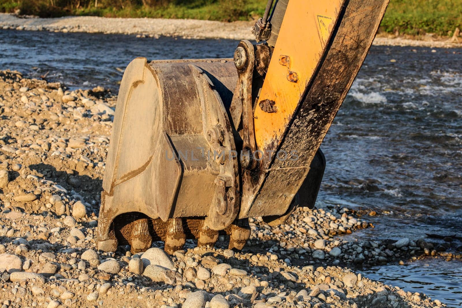 Digger (excavator machine) bucket digging stones ground by the river.