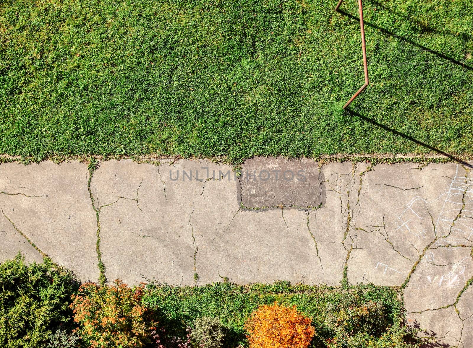 Old cracked pavement with green lawn and small bushes around. View from above, balcony on high floor flat.