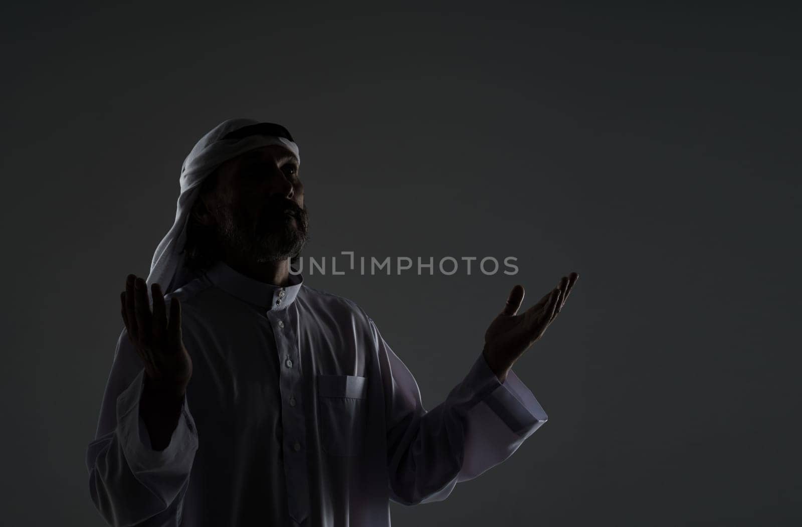 Muslim Arab man captures his spiritual devotion and faith as he prays, with hands raised to face in contemplation. Copy space for designers and publishers, black and white mid-length portrait by LipikStockMedia