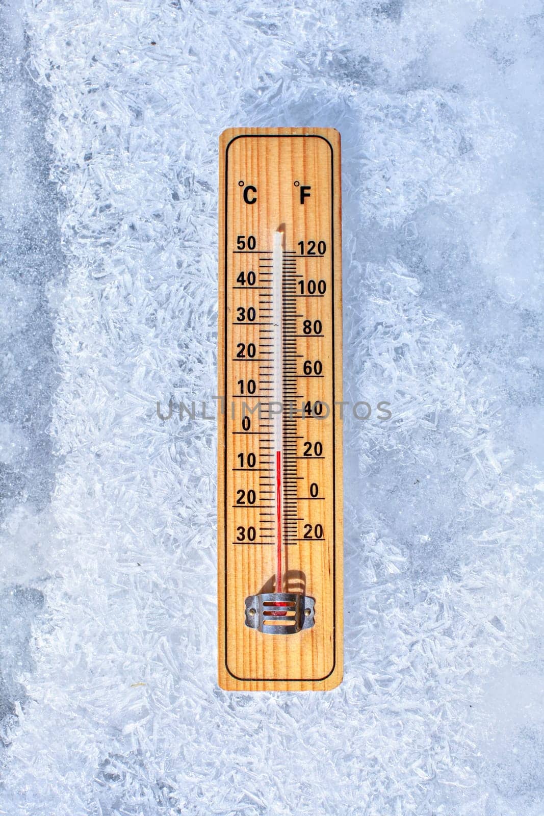 Thermometer laying on ice, showing minus 5 degrees. Sun shining from side. Winter / low temperatures coming, concept. by Ivanko