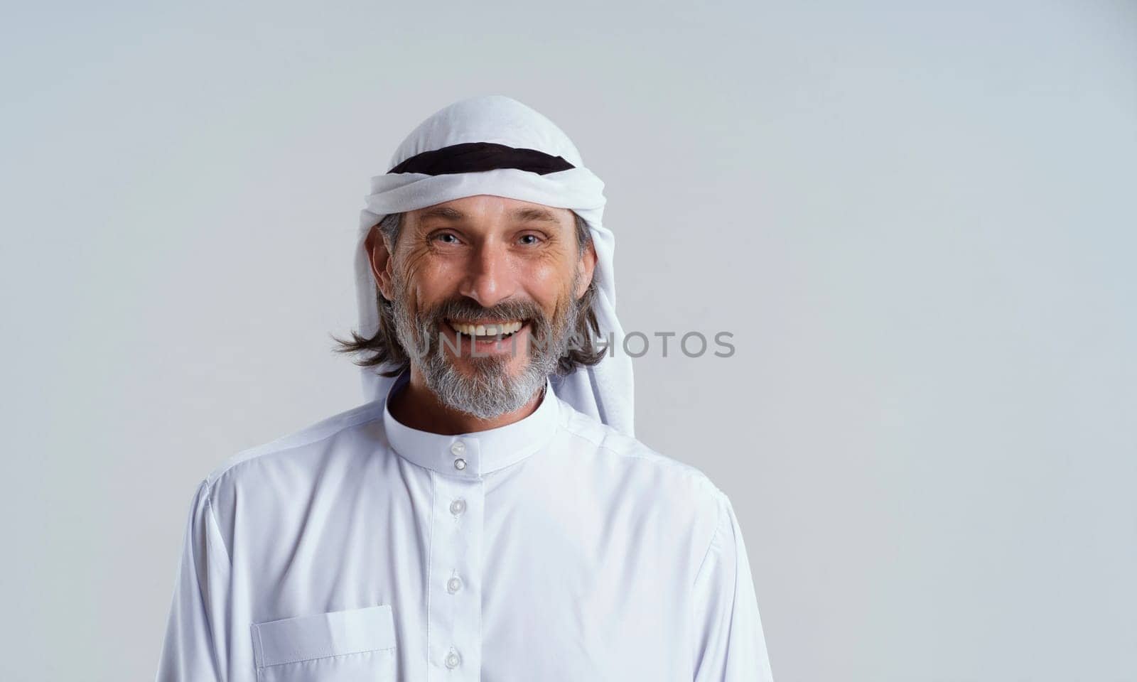 Smiling, happy Arab man in dishdasha, traditional clothing worn by Muslim men in the Middle East, isolated on white background with copy space. Man in headwear and has beard. mid length portrait. High quality photo