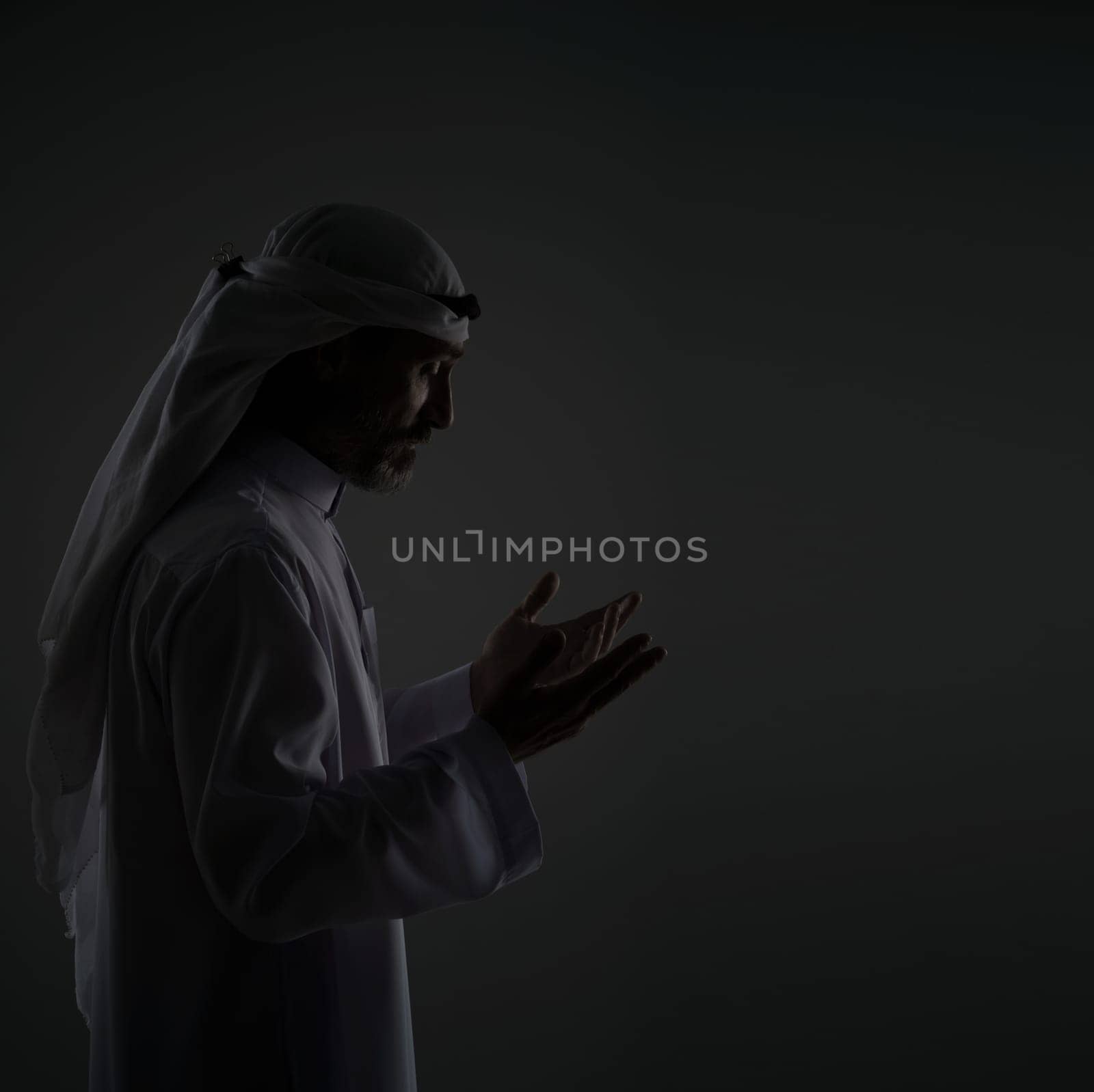 Muslim Arab man is prayer, raising hands to face with peaceful, serene expression. Copy space and portrays the man's devotion and spirituality in traditional Islamic context. Black and white portrait by LipikStockMedia
