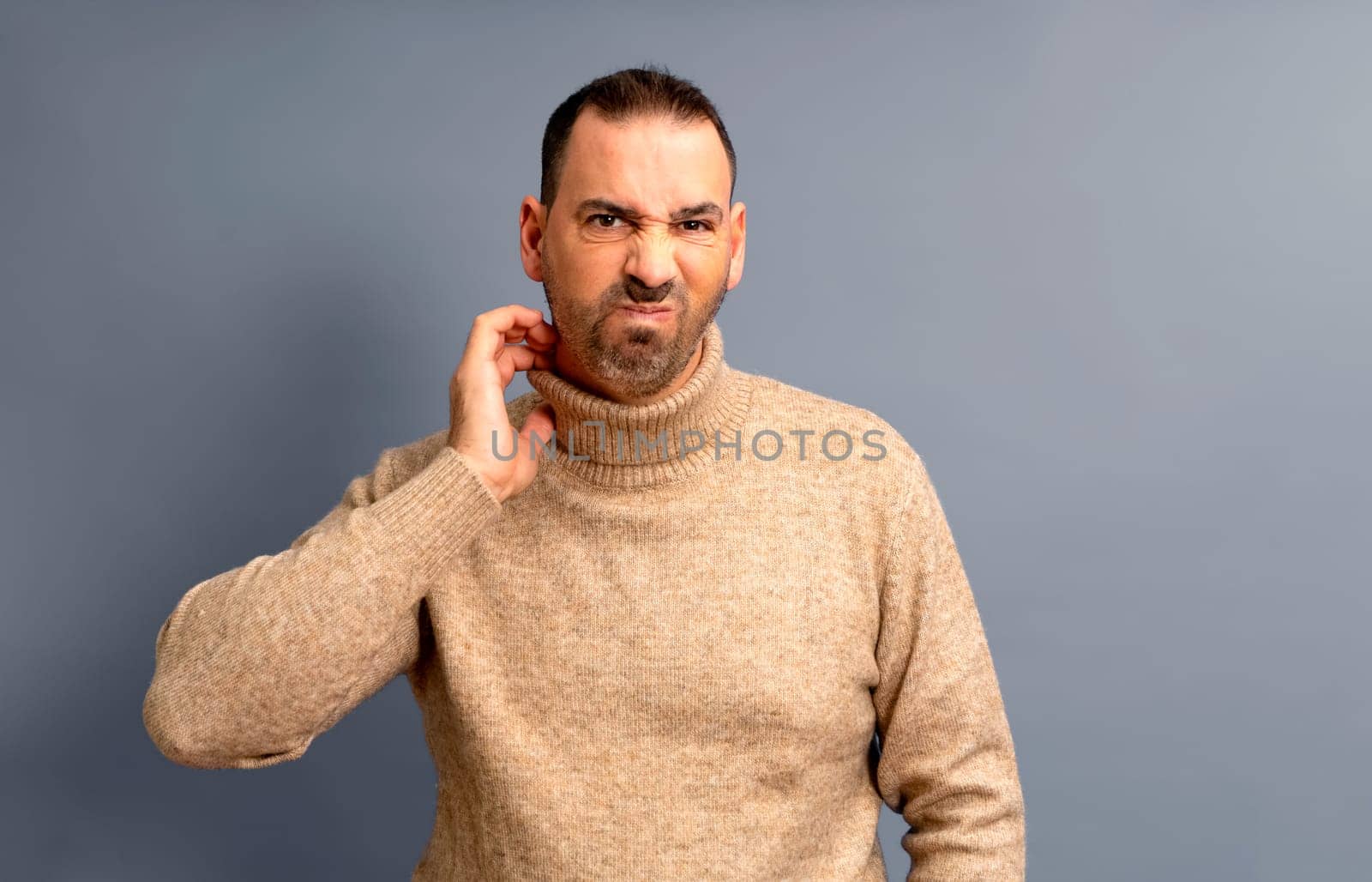 Middle age bearded man scratching himself highlighted with red collar on gray studio background, copy space. Upset man suffering from itchy, rash on his neck. Allergic reaction, eczema concept