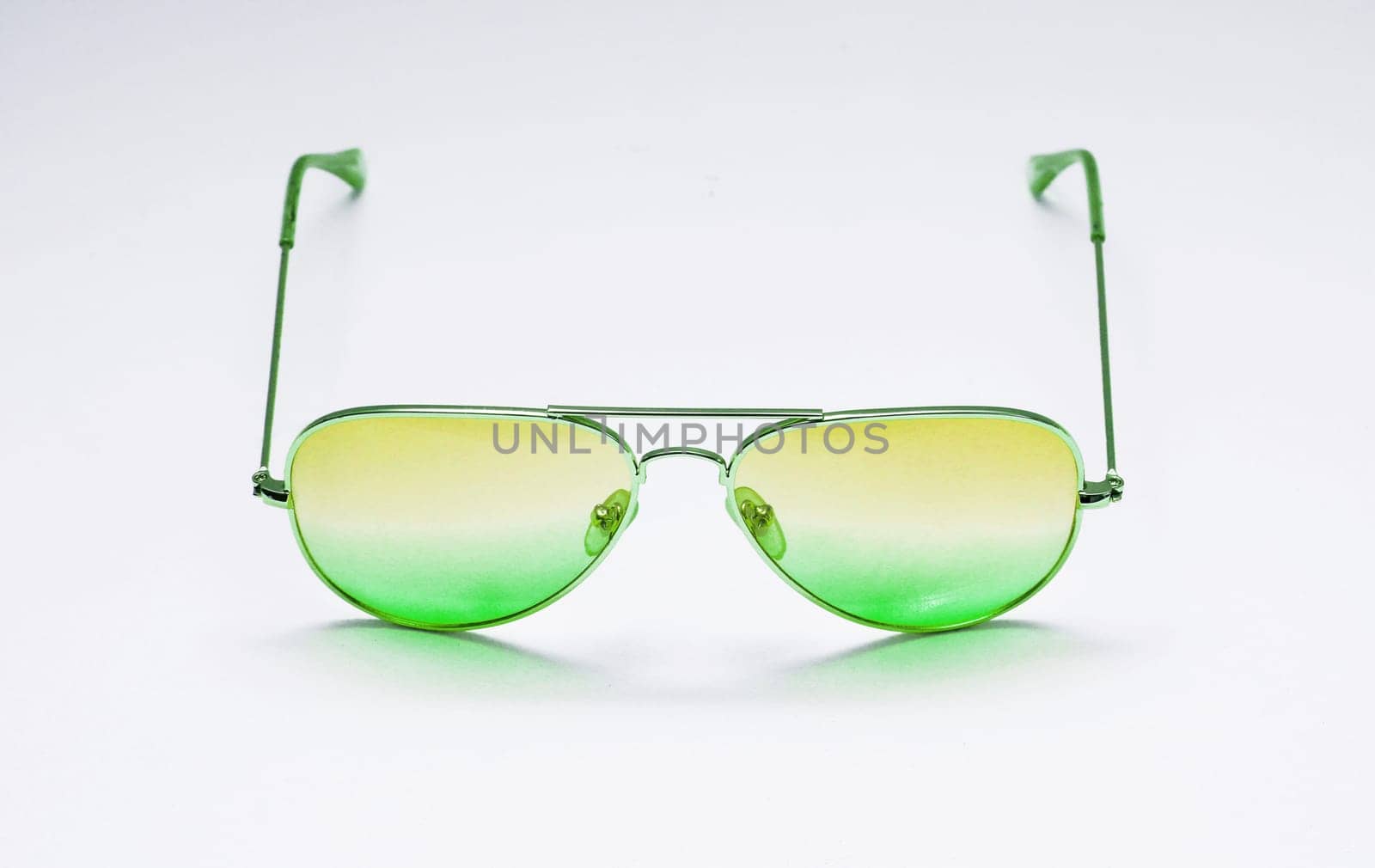 Thin-rimmed glass sunglasses with a green gradient against a white wall close-up.