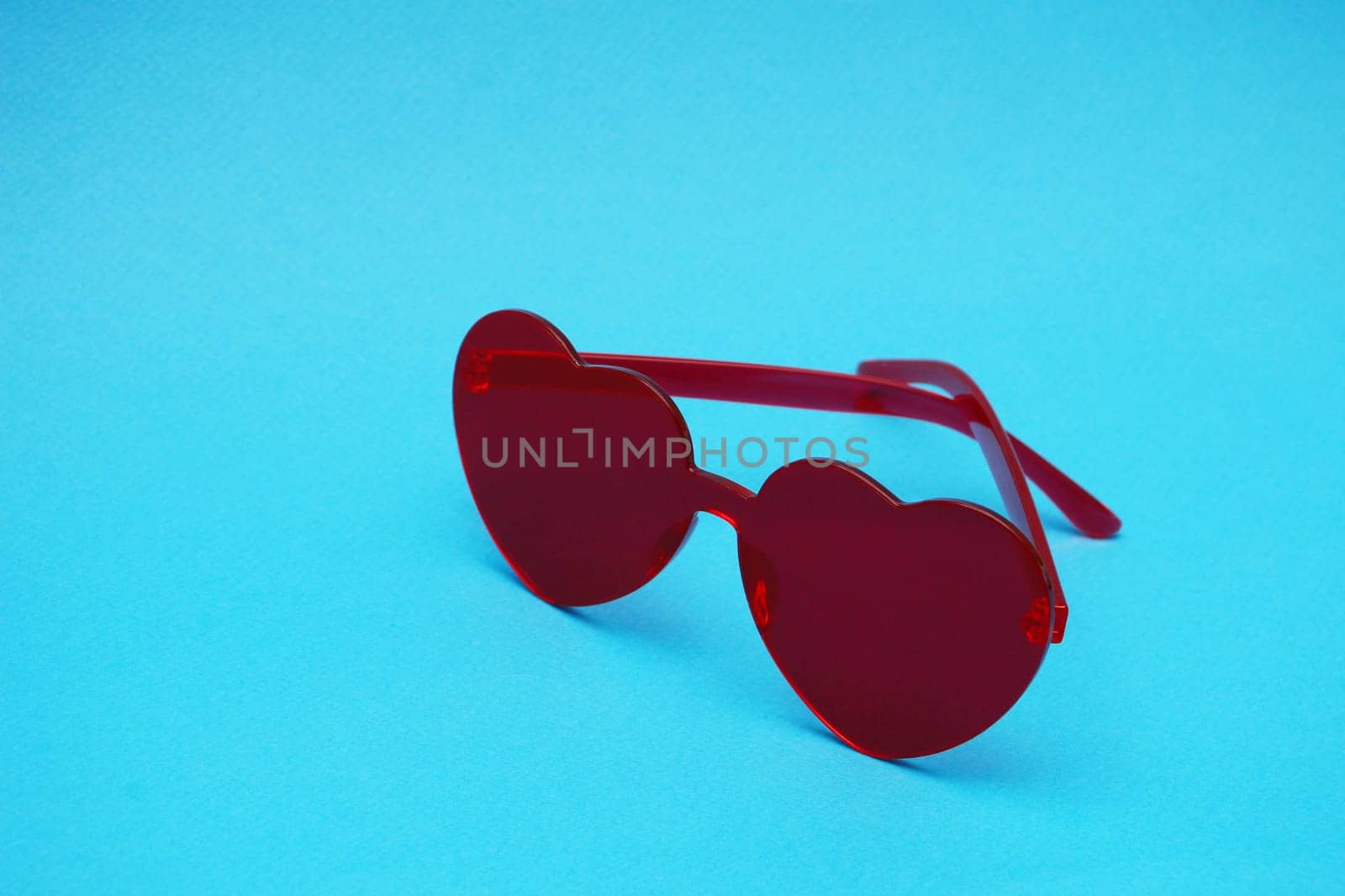 Red sunglasses in the shape of a heart on a blue background. ..Elegant red plastic glasses in the shape of a heart on a blue paper background close-up.