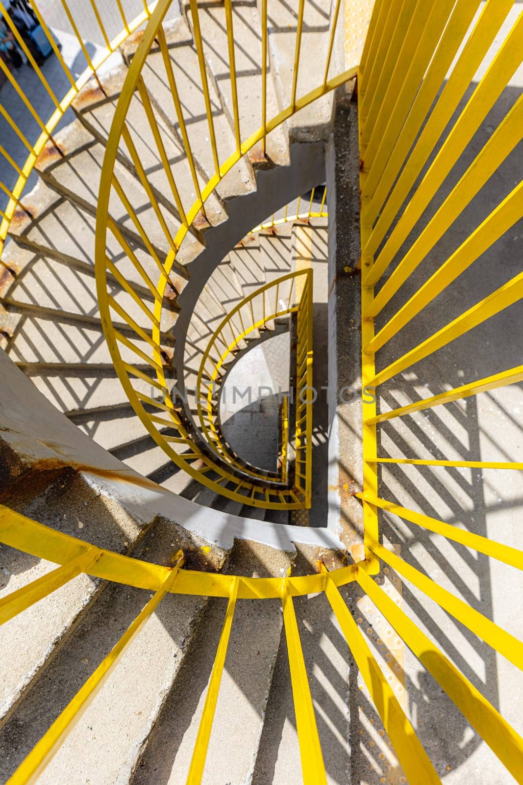 Top view of a concrete spiral staircase with yellow railings on a sunny morning by Wierzchu