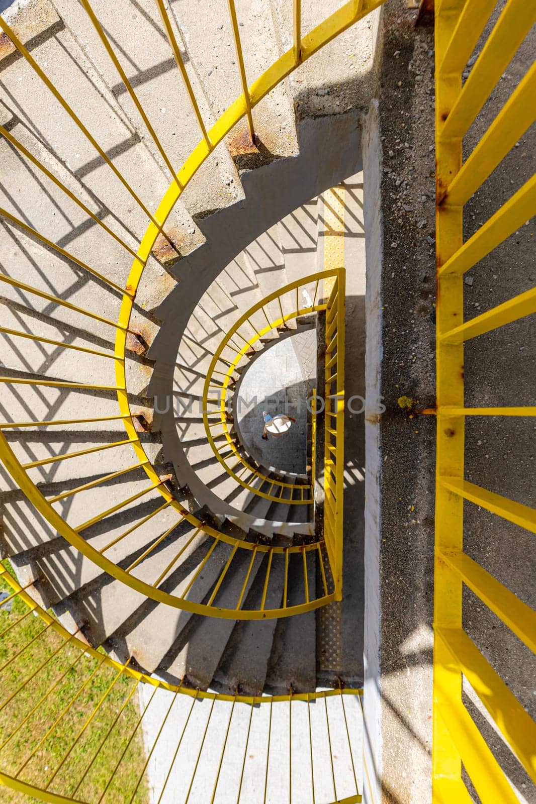 Top view of a concrete spiral staircase with yellow railings on a sunny morning by Wierzchu