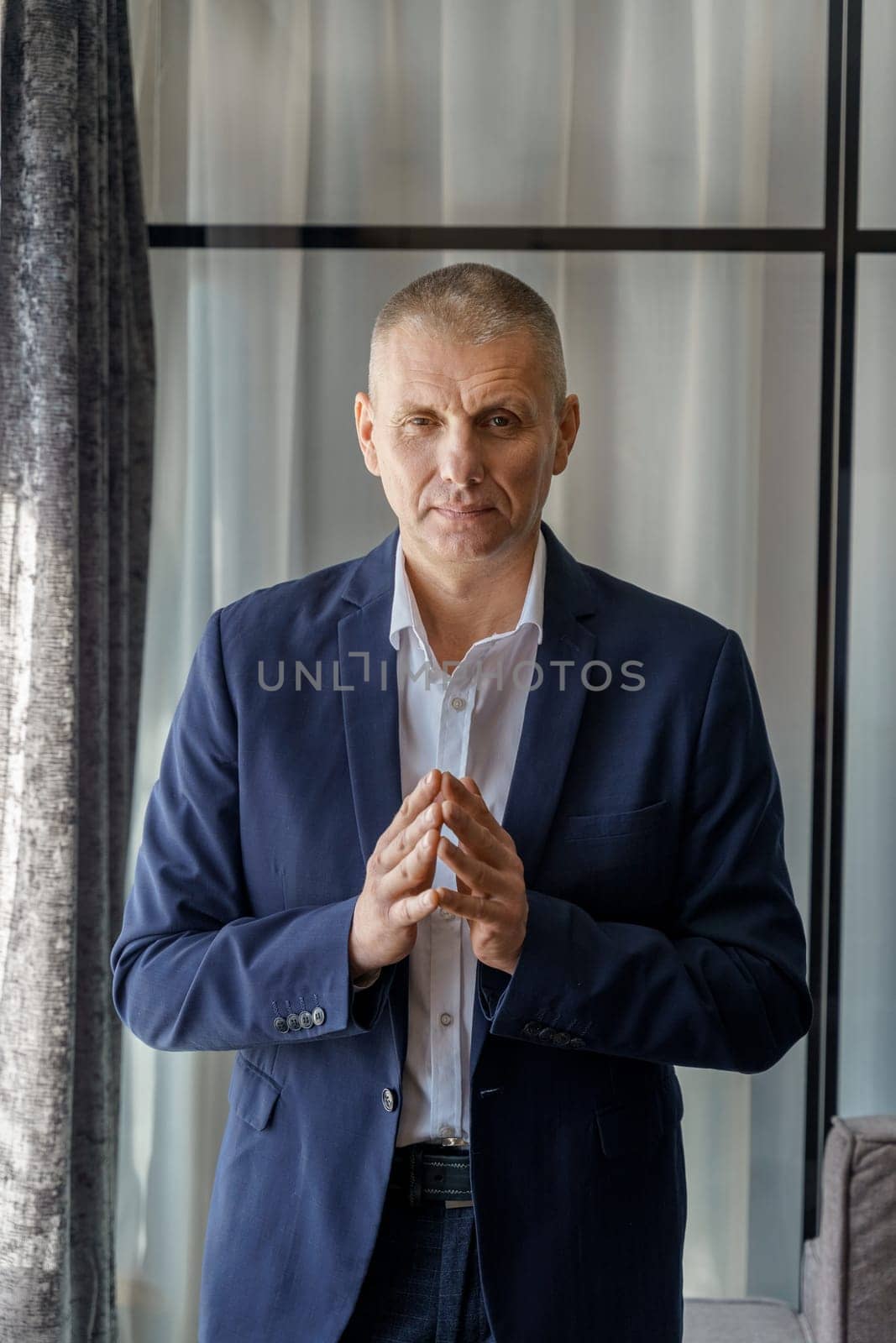 Portrait of a mature calm businessman with his jacket unbuttoned and palms folded in front.