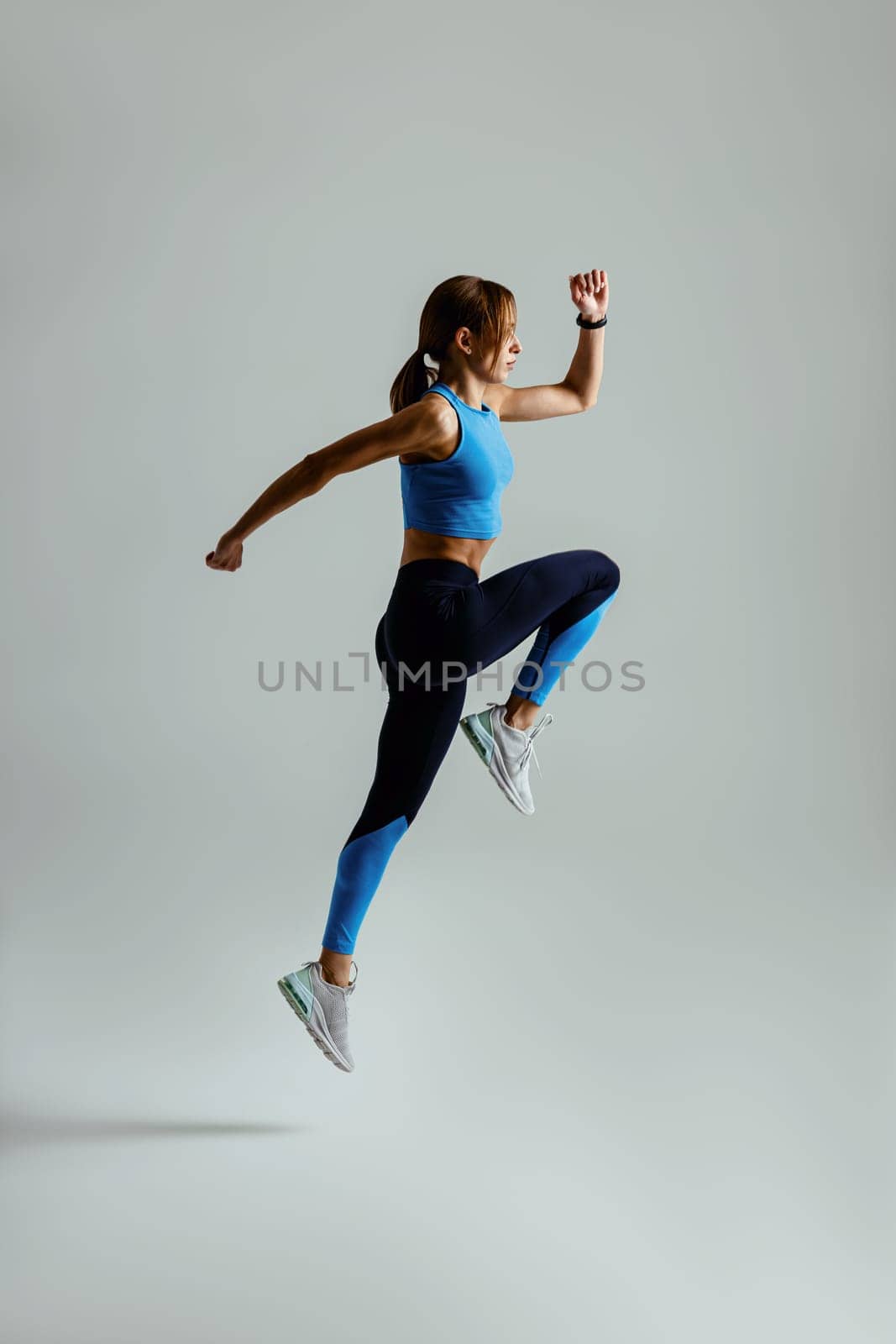 Sporty determined woman running in Mid-Air exercising during cardio workout over studio background by Yaroslav_astakhov