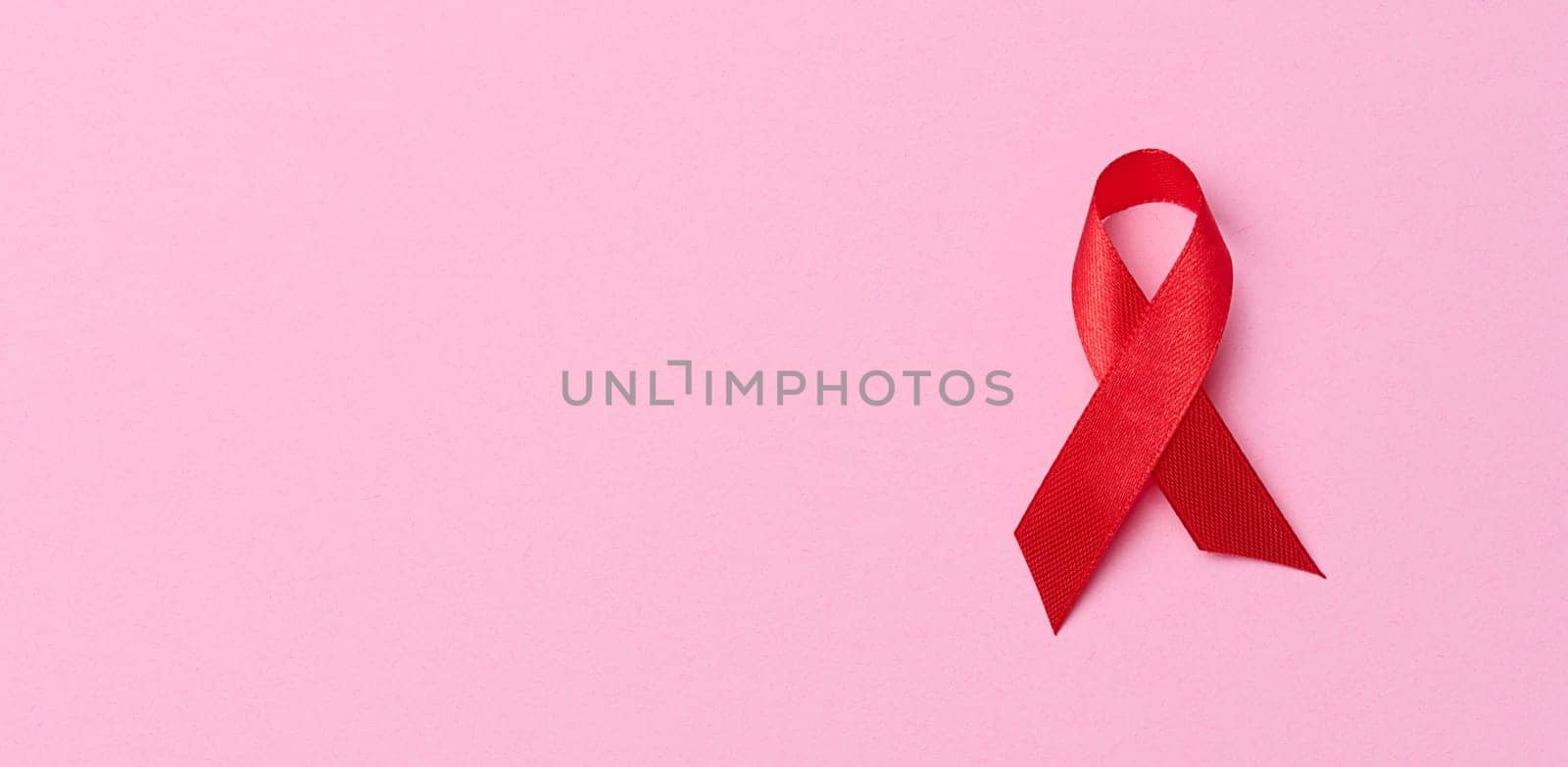 A silk red ribbon in the form of a bow on a pink background, a symbol of the fight against AIDS and a sign of solidarity and support