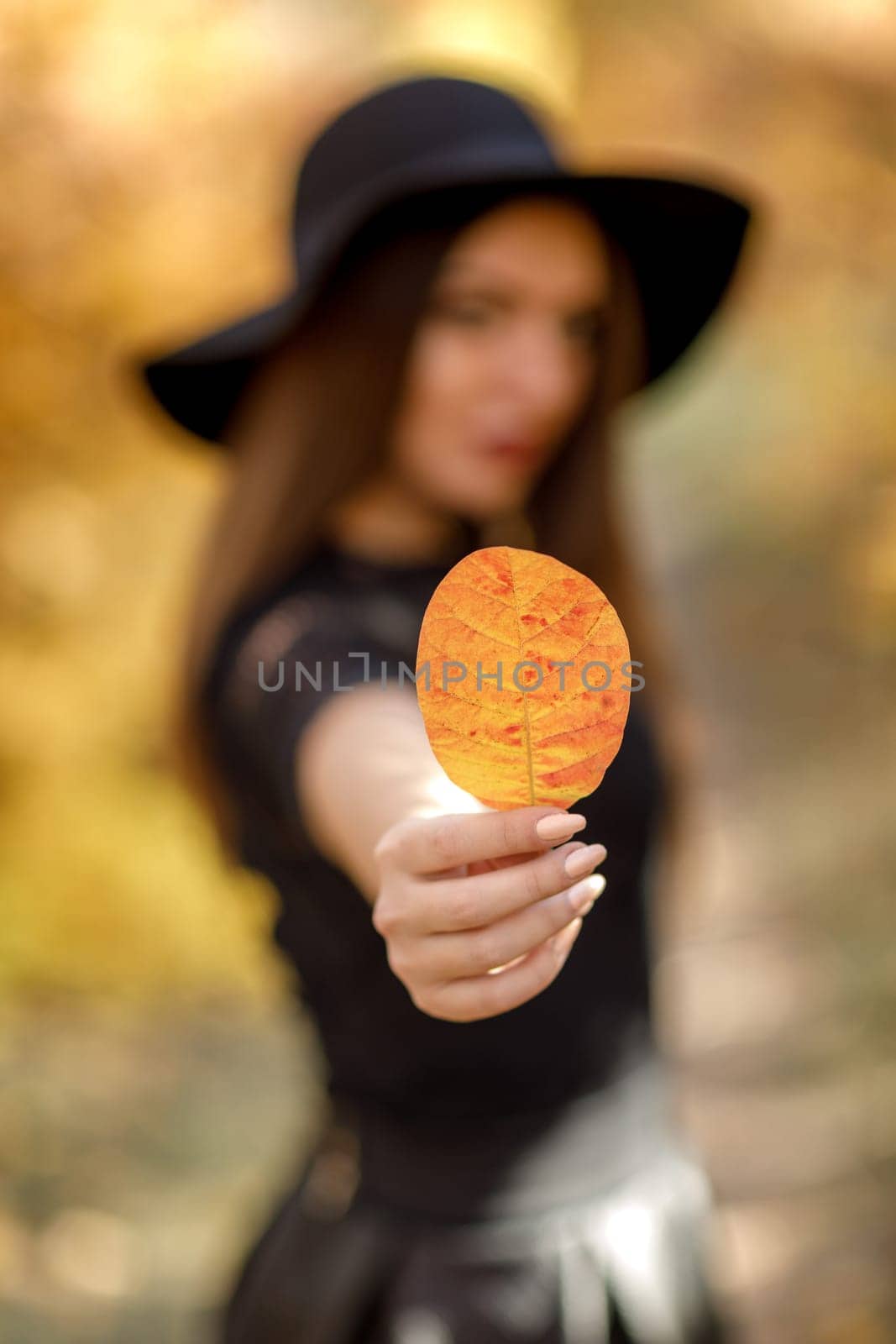 portrait of beautiful woman in black hat with yellow autumn leaf. focus on leaf