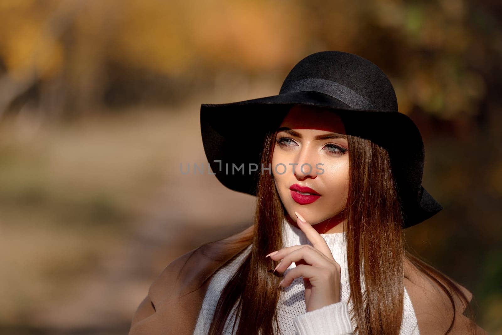 portrait of beautiful young woman in black hat in park in the autumn