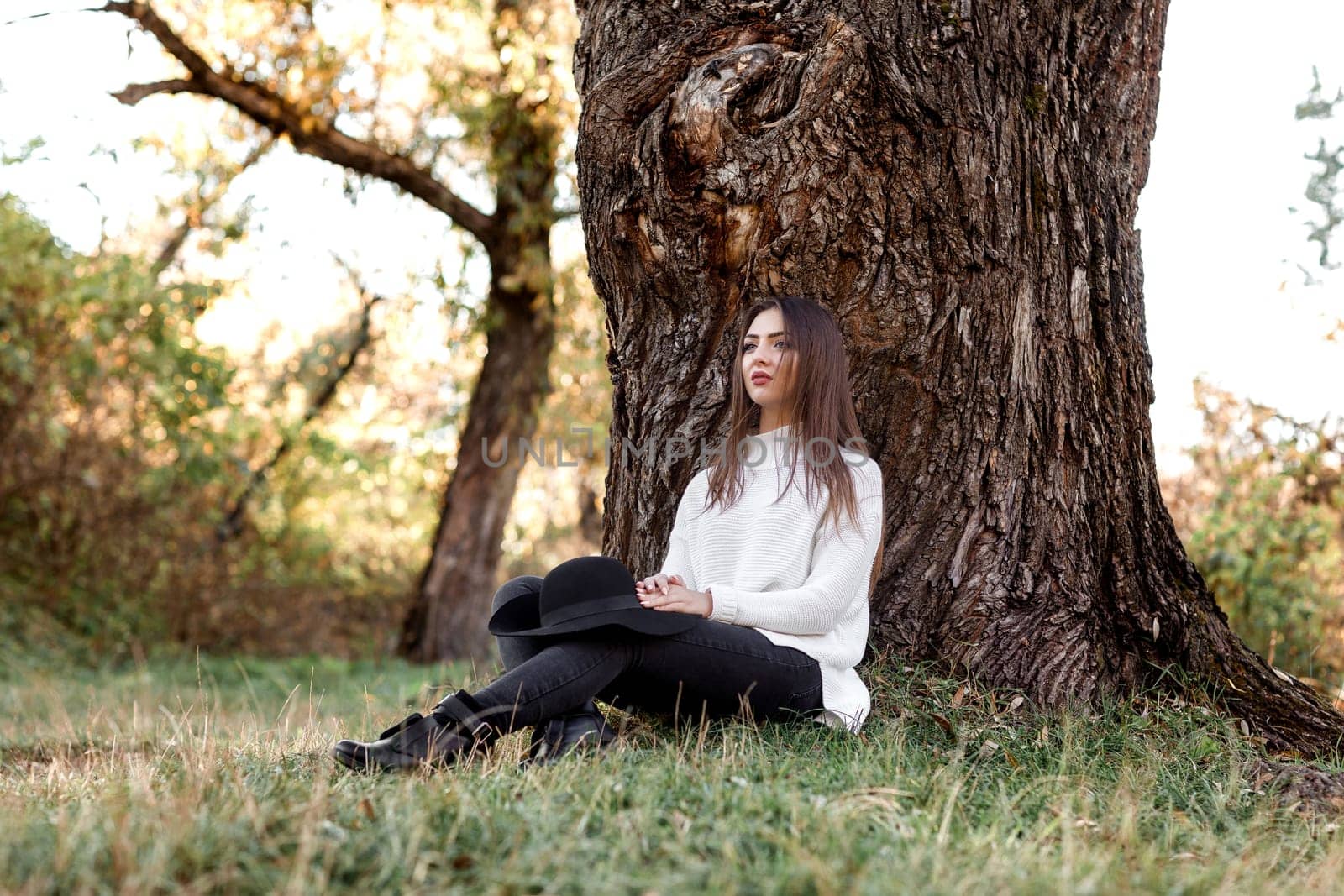 beautiful woman sitting under big tree and daydreaming on sunny autumn day.