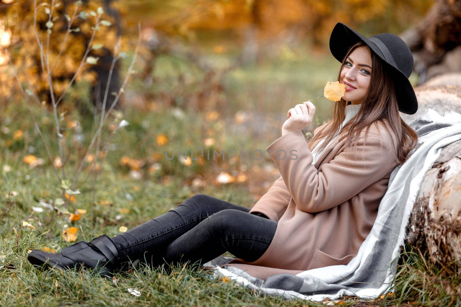 beautiful woman in black hat sitting near tree and dreams on sunny autumn day.