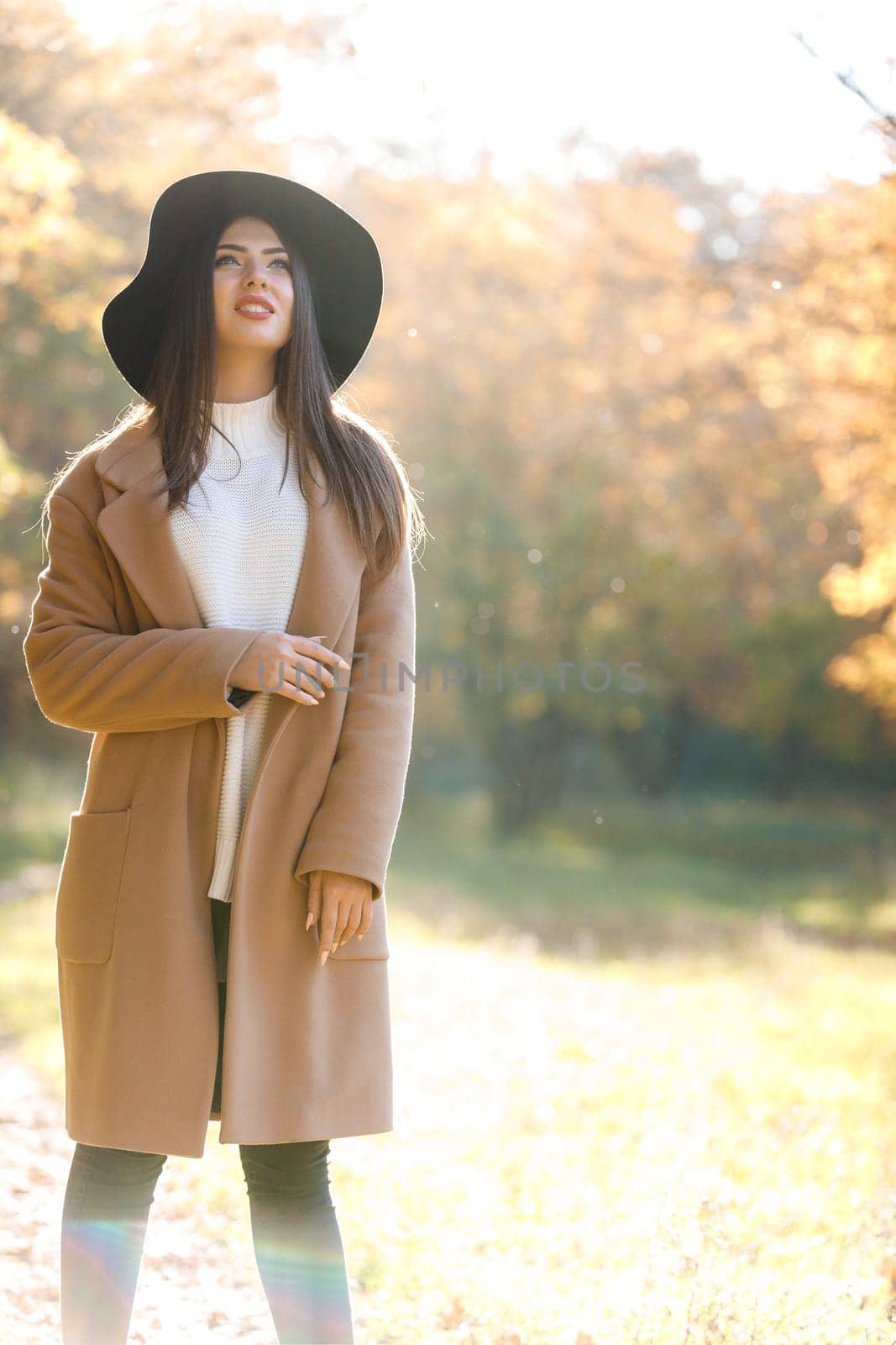 beautiful young woman in coat and black hat in park in the autumn. high key