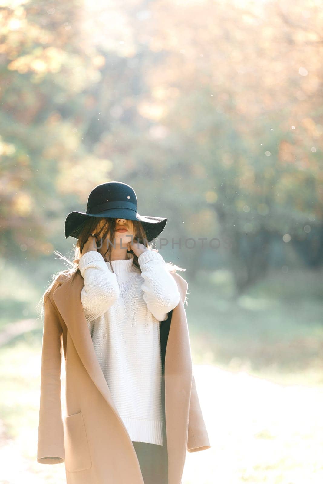 beautiful young woman in coat and black hat in park by erstudio