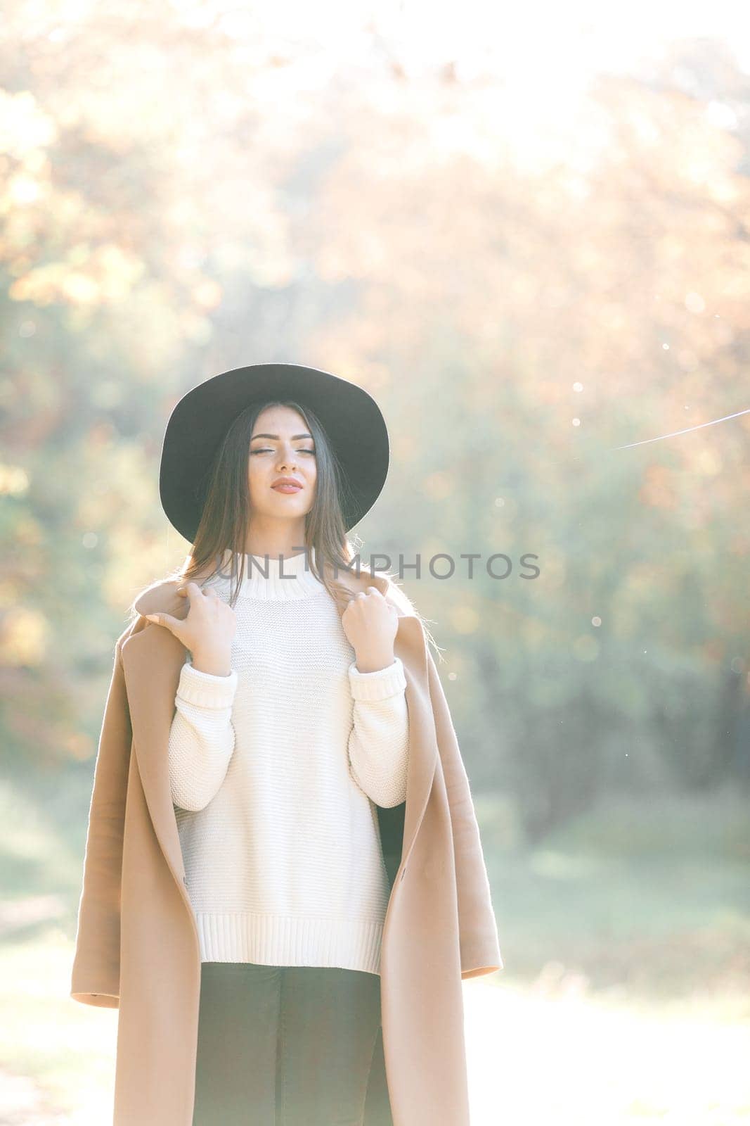 beautiful young woman in coat and black hat in park by erstudio