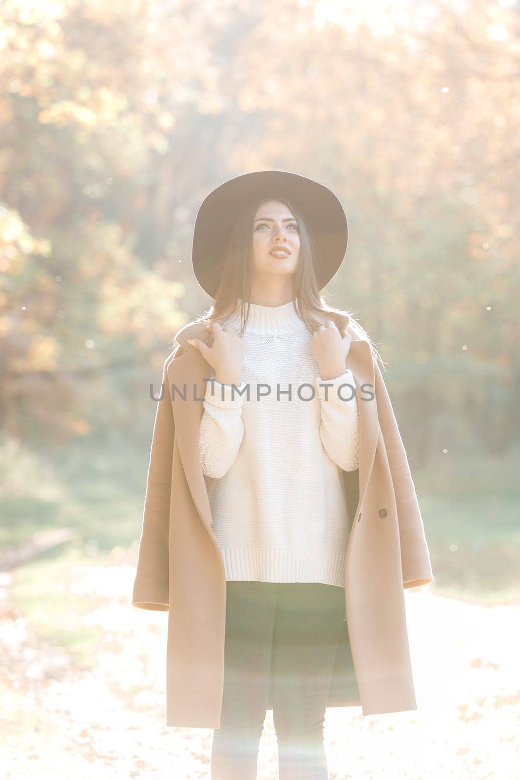 beautiful young woman in coat and black hat in park by erstudio