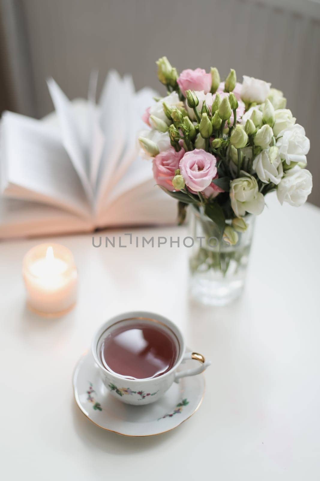 Romantic Spring still life. Romantic background with cup of tea, rose flowers and open book over white table
