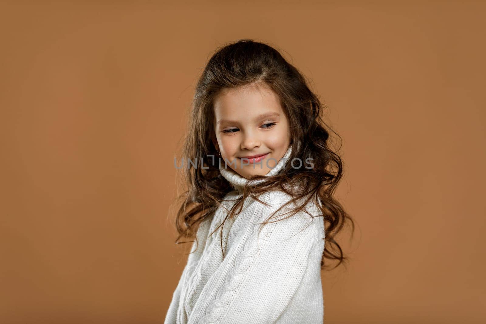 Cute shy little child girl in white sweater on beige background. Human emotions