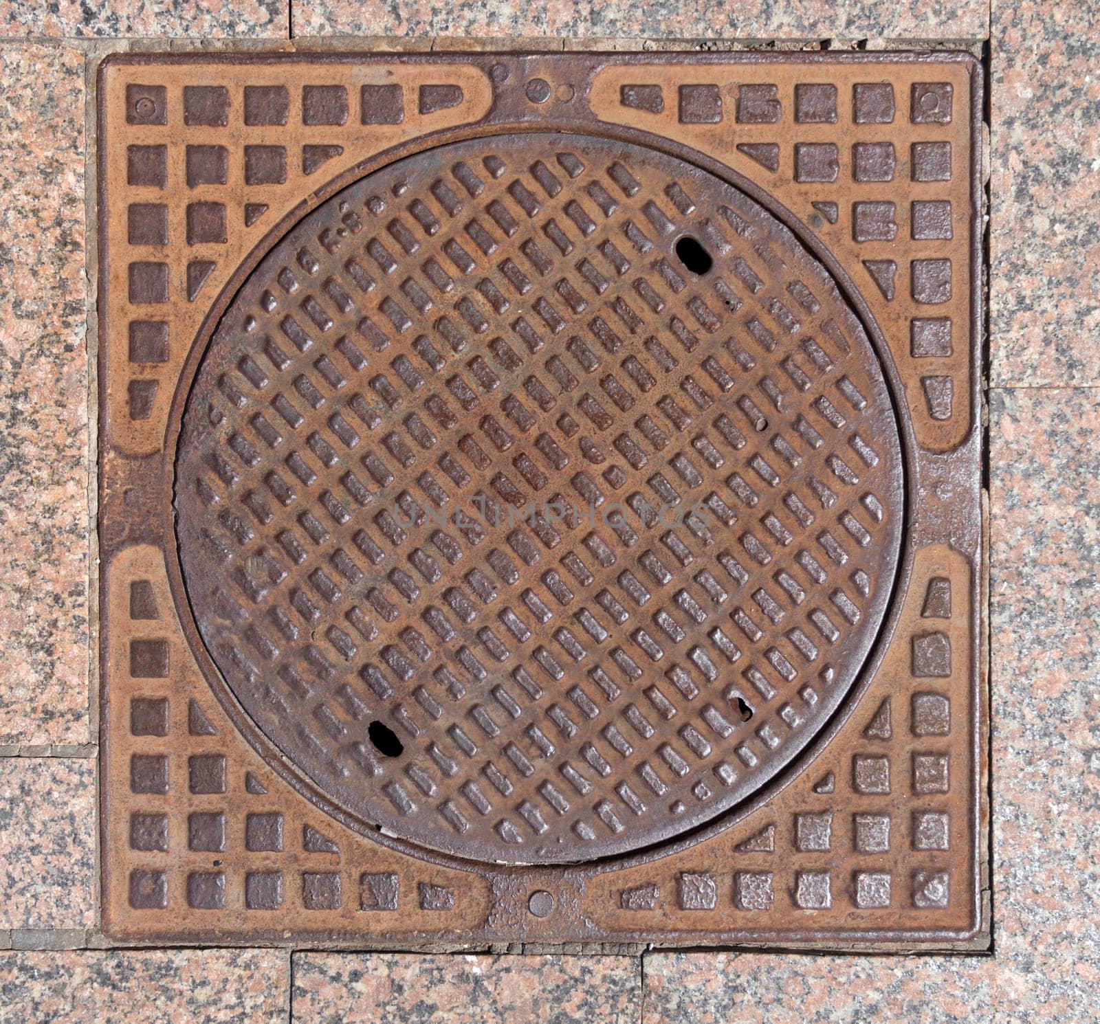 Old rusty sewer hatch on an old metal plate. View from above.