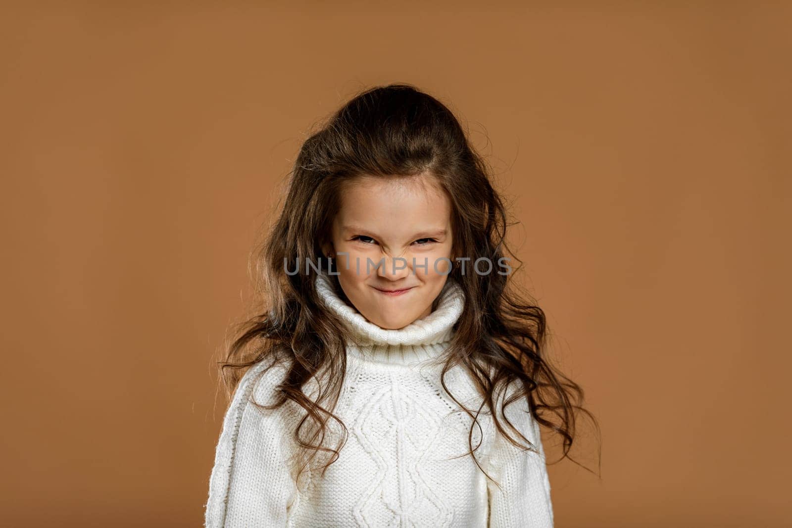 frowned little child girl in white sweater looking to camera. Human emotions and facial expression