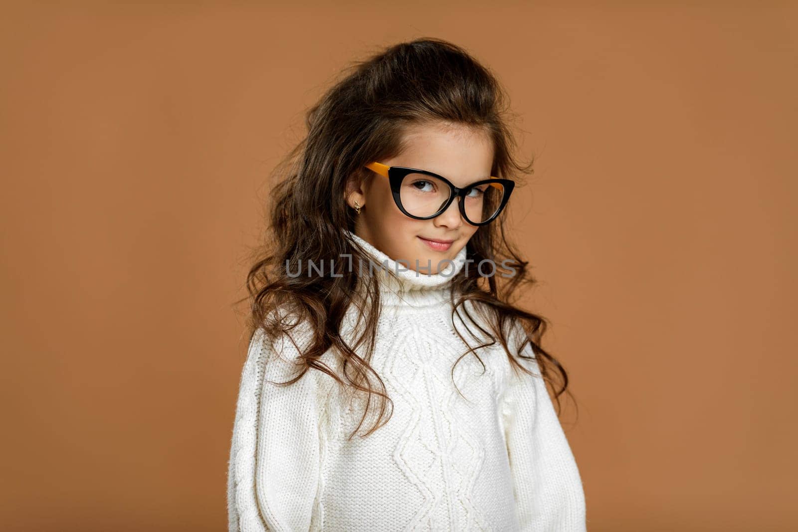 Cute curly little child girl wearing glasses and looking to camera in studio